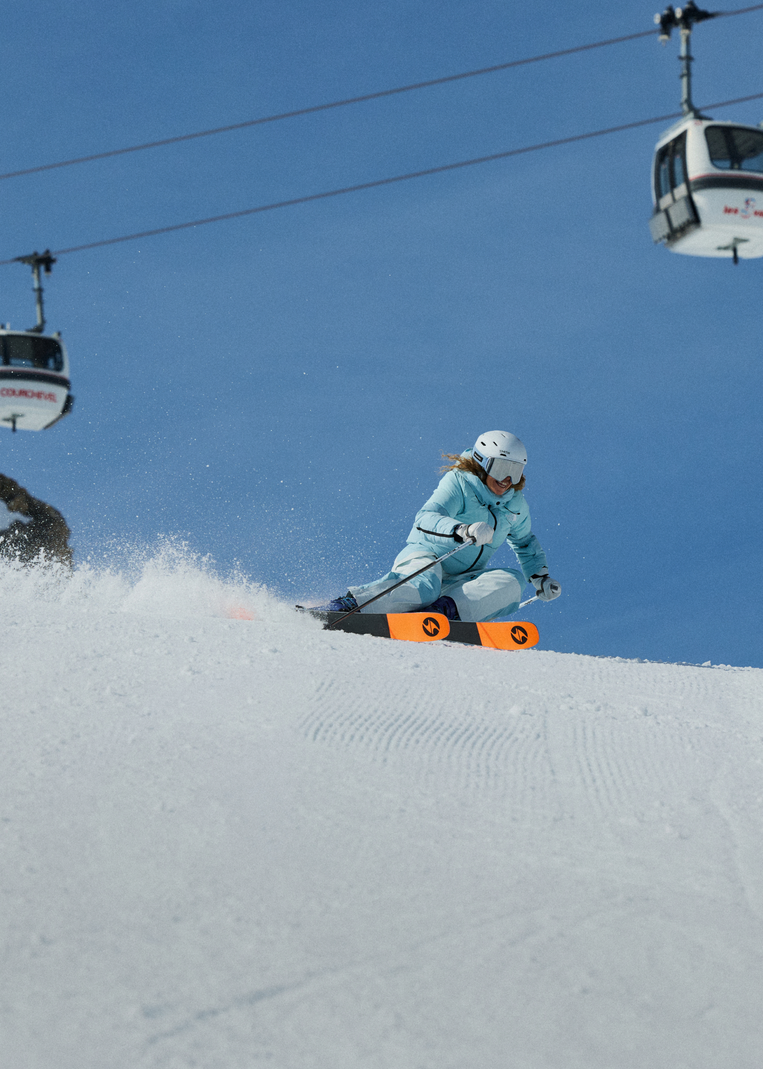 A skier in blue gear navigates a snowy slope under a clear sky with cable cars above.