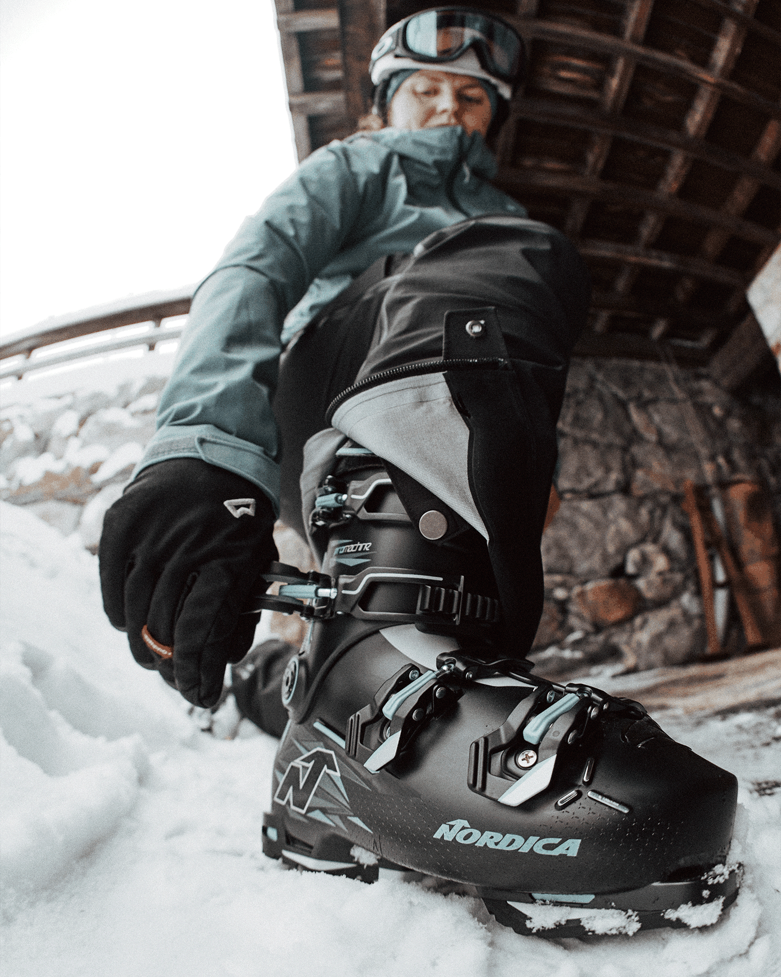 Person fastening ski boot buckles in a snowy outdoor setting, wearing a helmet and gloves.