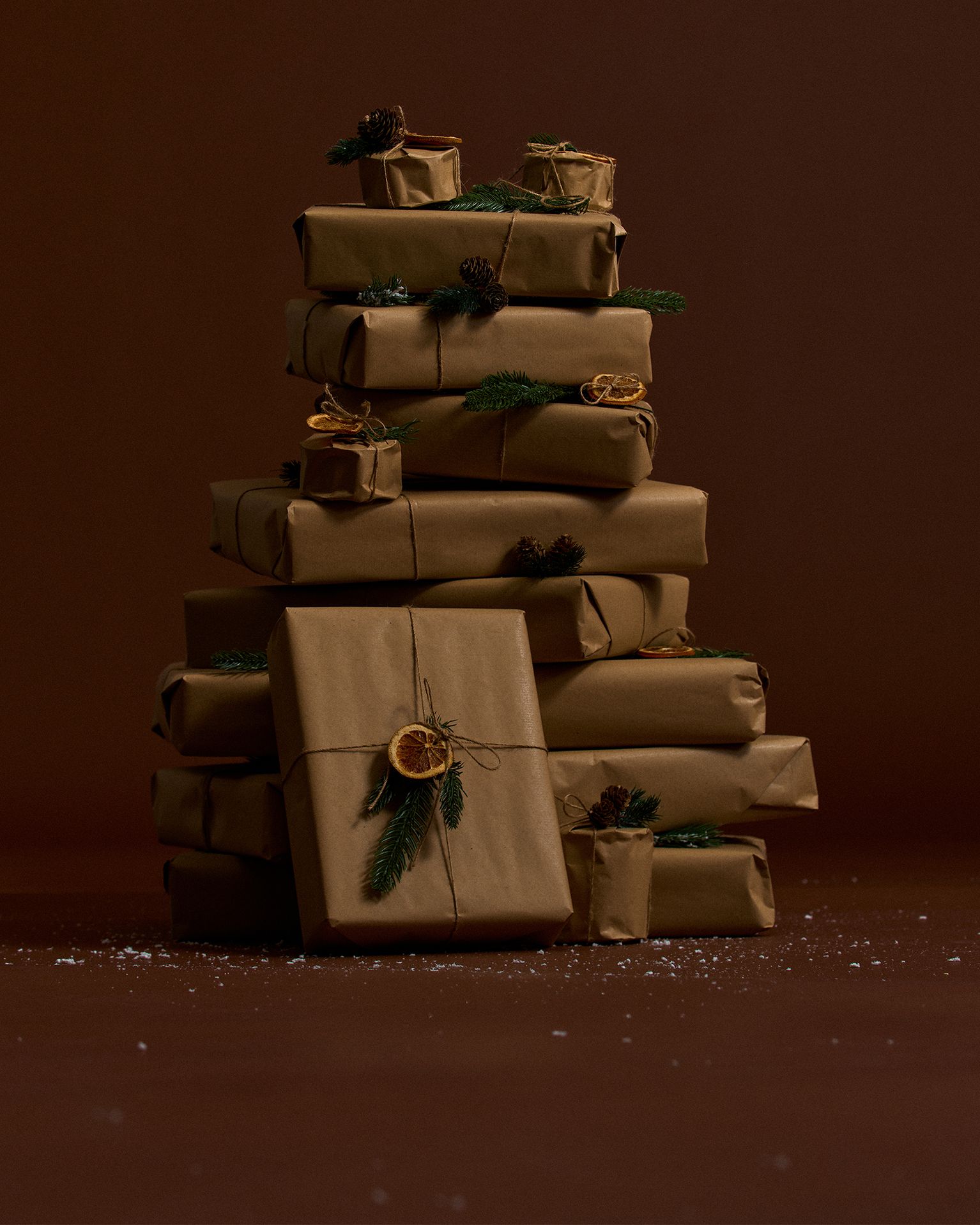 A stack of brown paper-wrapped gifts adorned with pine branches and dried orange slices, set against a dark background.