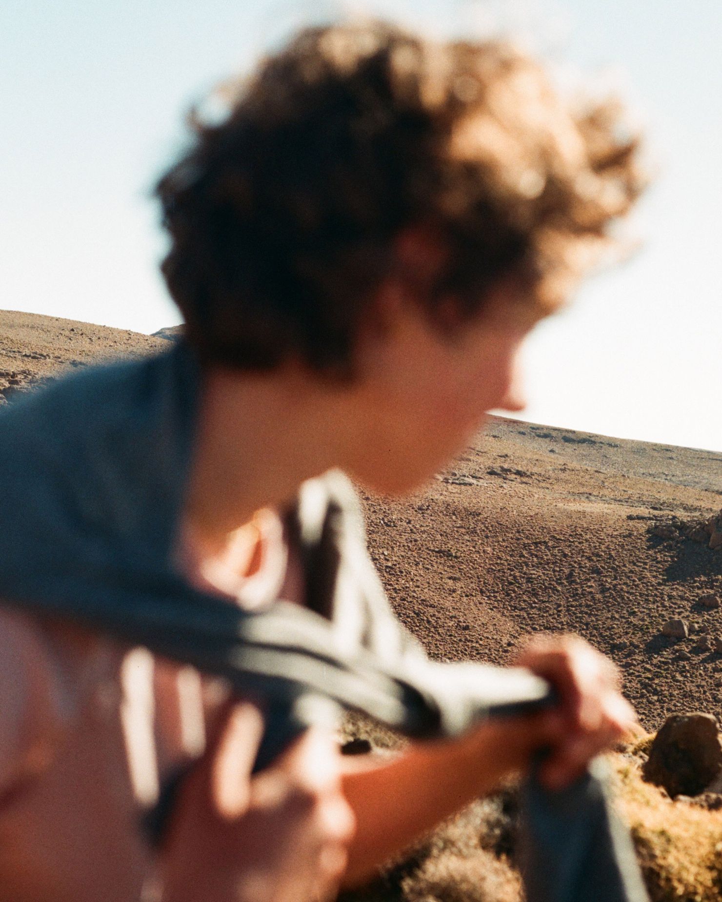Person holding a jacket stands in a rugged, sunlit mountain landscape, with blurred focus on their figure.