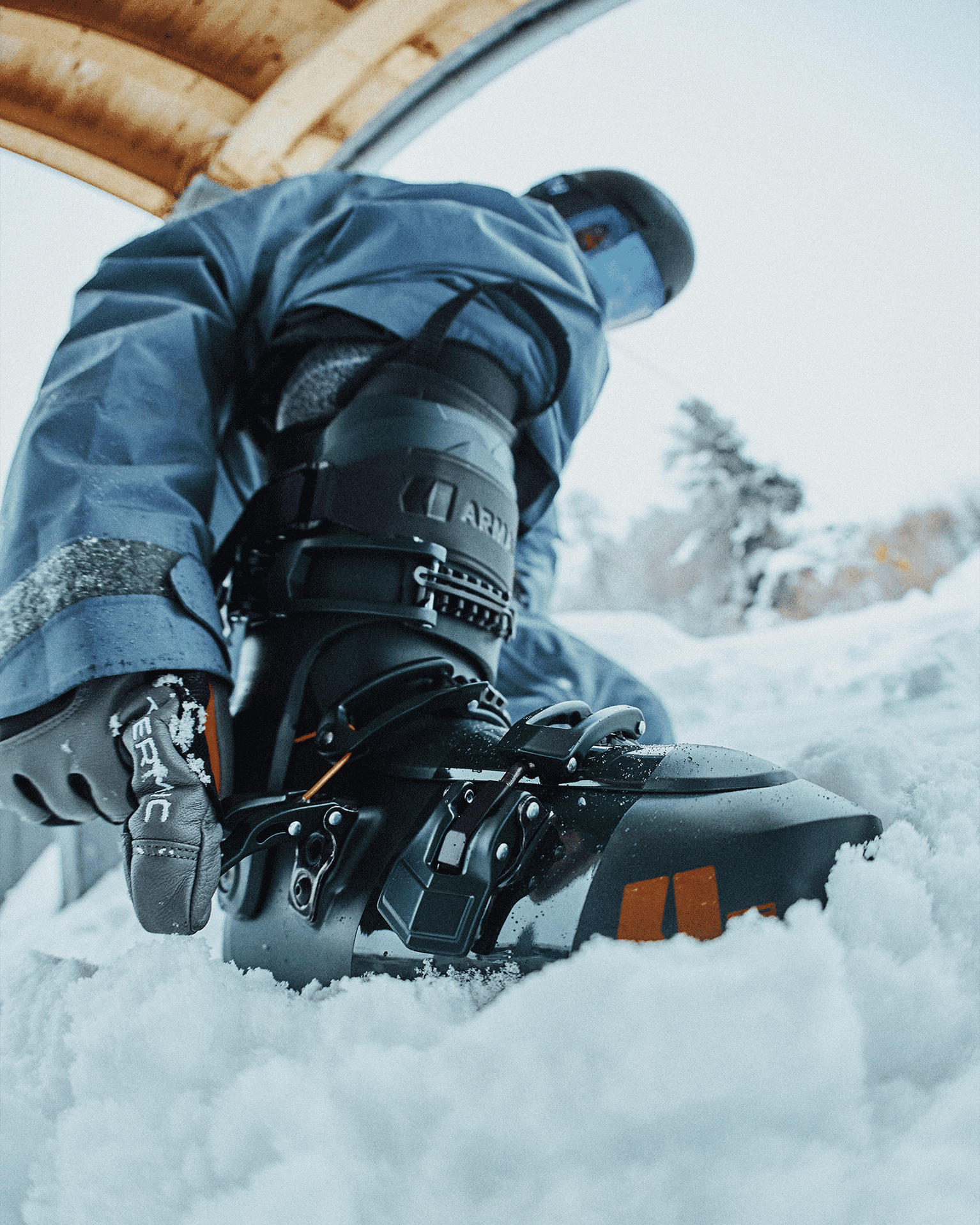 Person in snow gear adjusting ski boots in snowy environment.