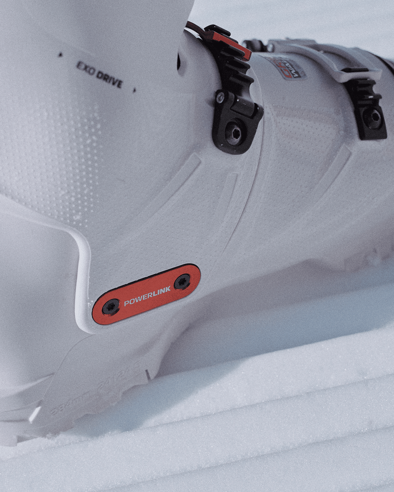 Close-up of a white ski boot with "EXO DRIVE" and "POWERLINK" features, resting on snow.