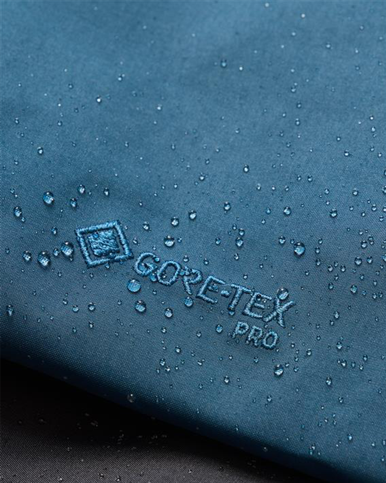 Close-up of blue GORE-TEX fabric with water droplets on the surface, showcasing its waterproof properties.