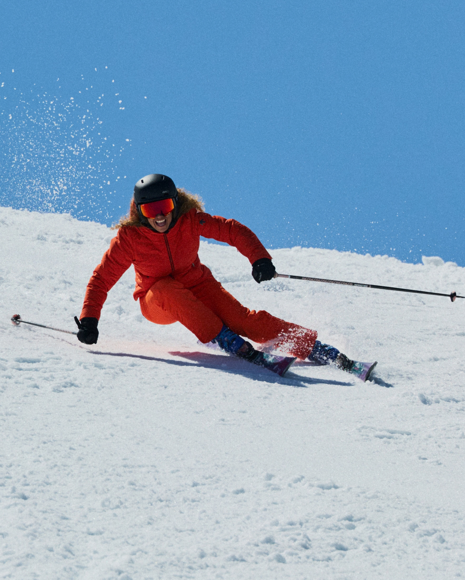 Skier in a bright red outfit expertly carving down a snowy slope under a clear blue sky.