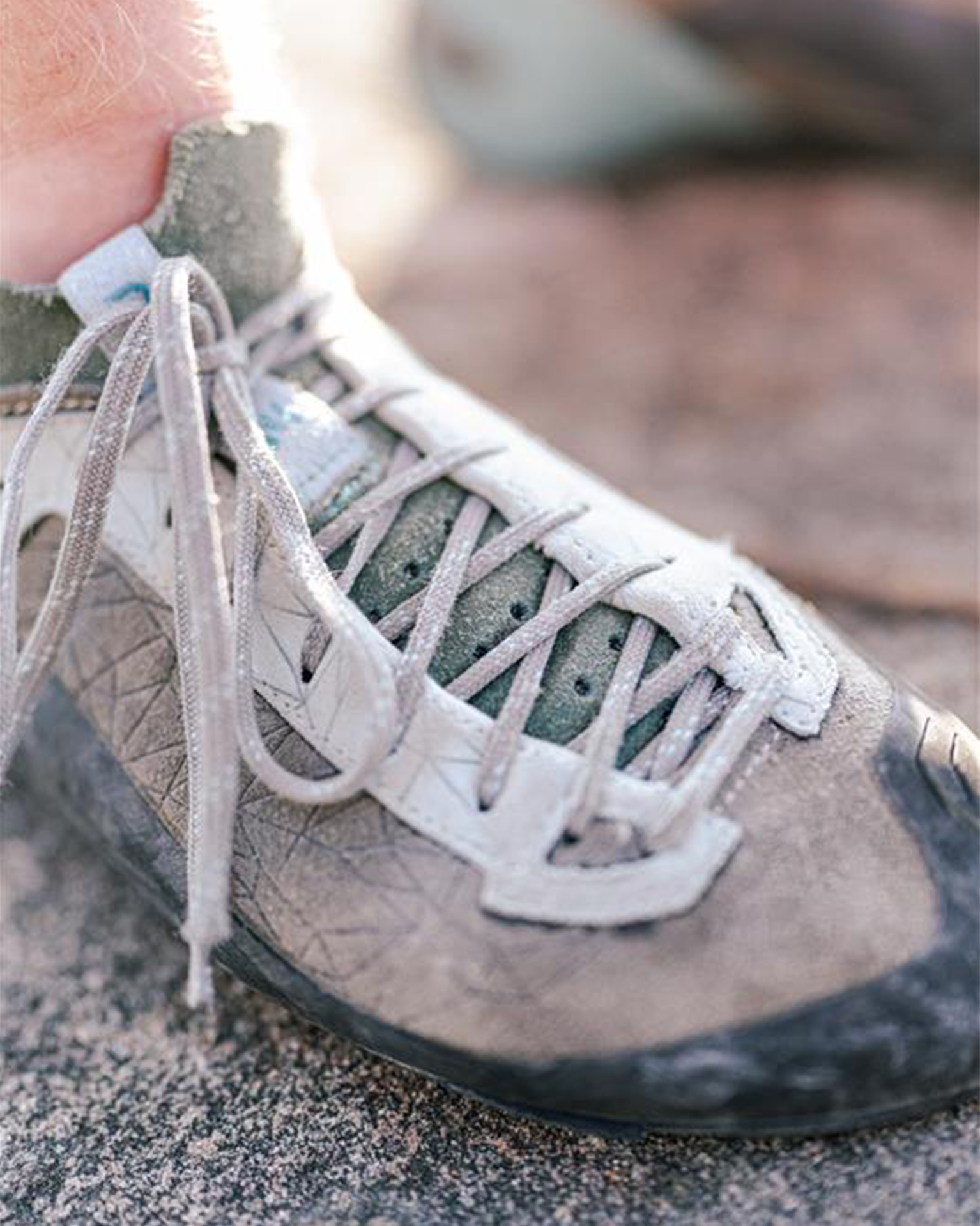 Close-up of a worn gray climbing shoe with intricate lacing, resting on a rough stone surface.