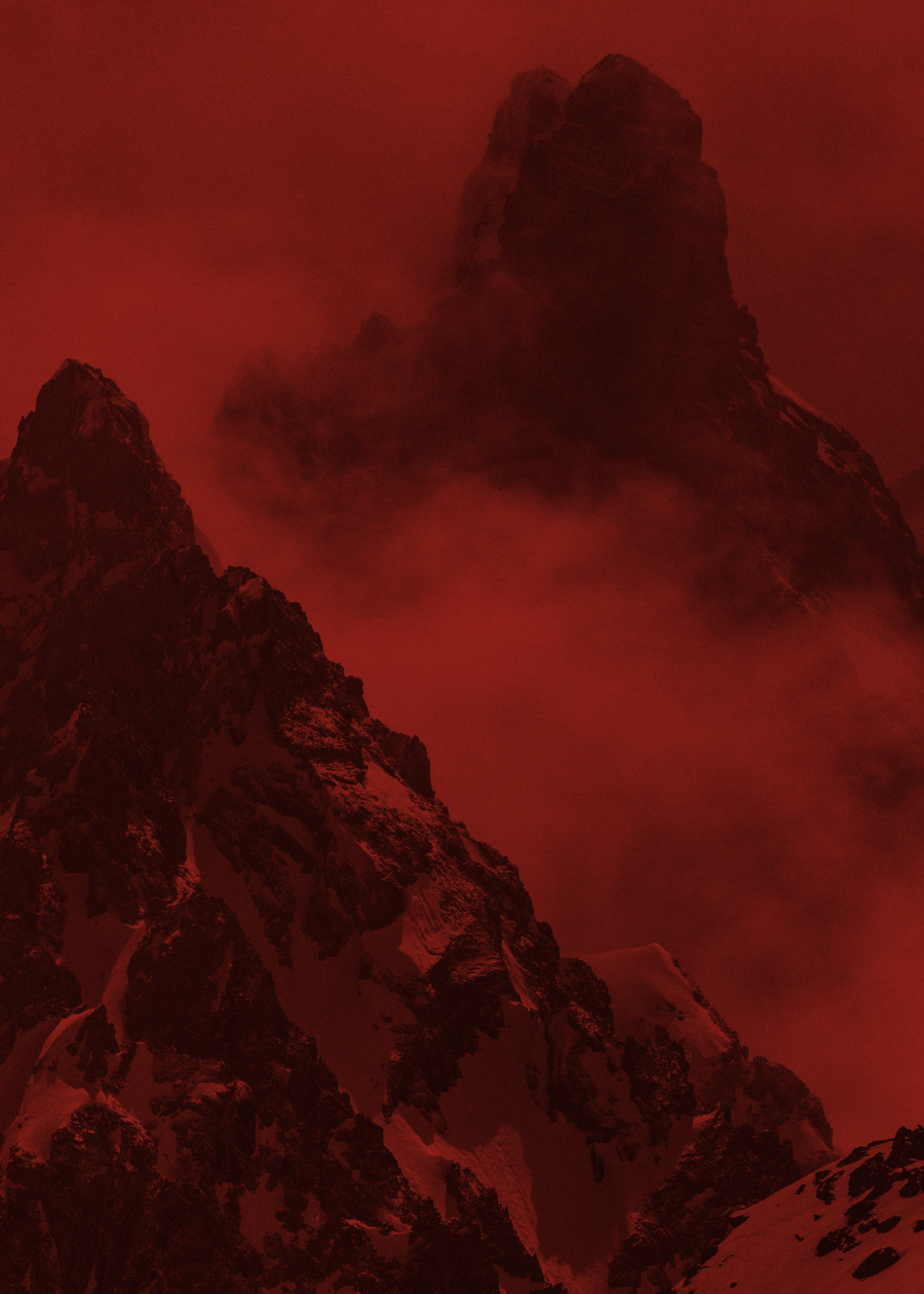 Dramatic, misty mountain peaks under a red-tinted sky, showcasing rugged terrain and steep slopes.
