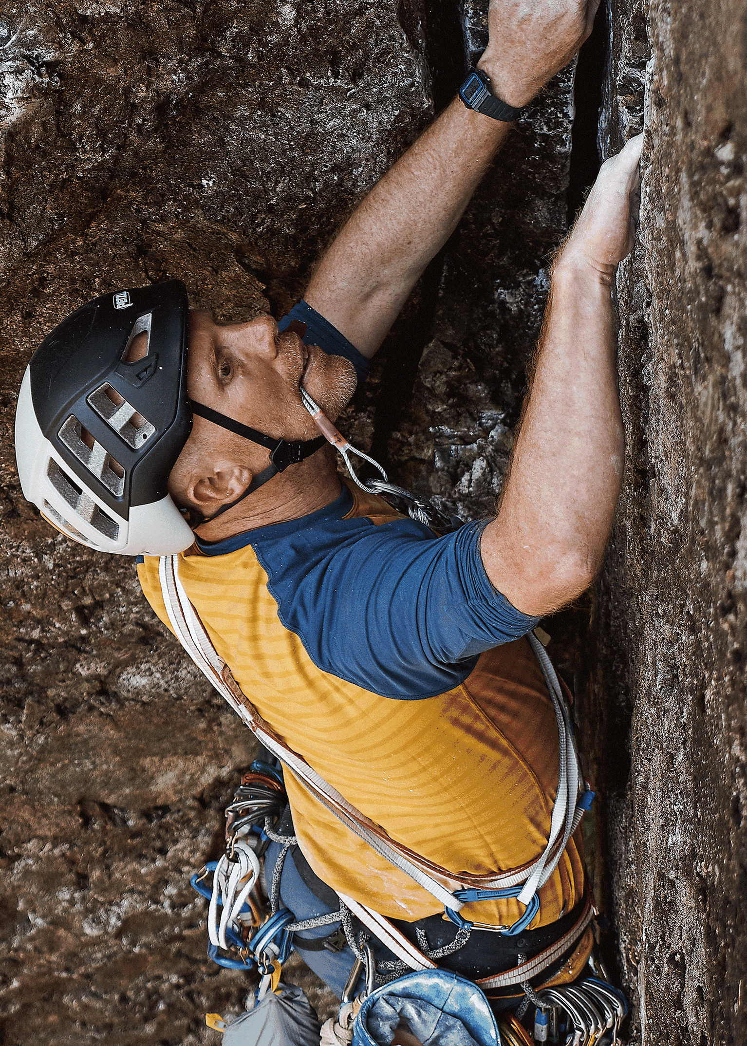 Climber in a helmet scales a rocky surface, using equipment, focused and determined in his ascent.
