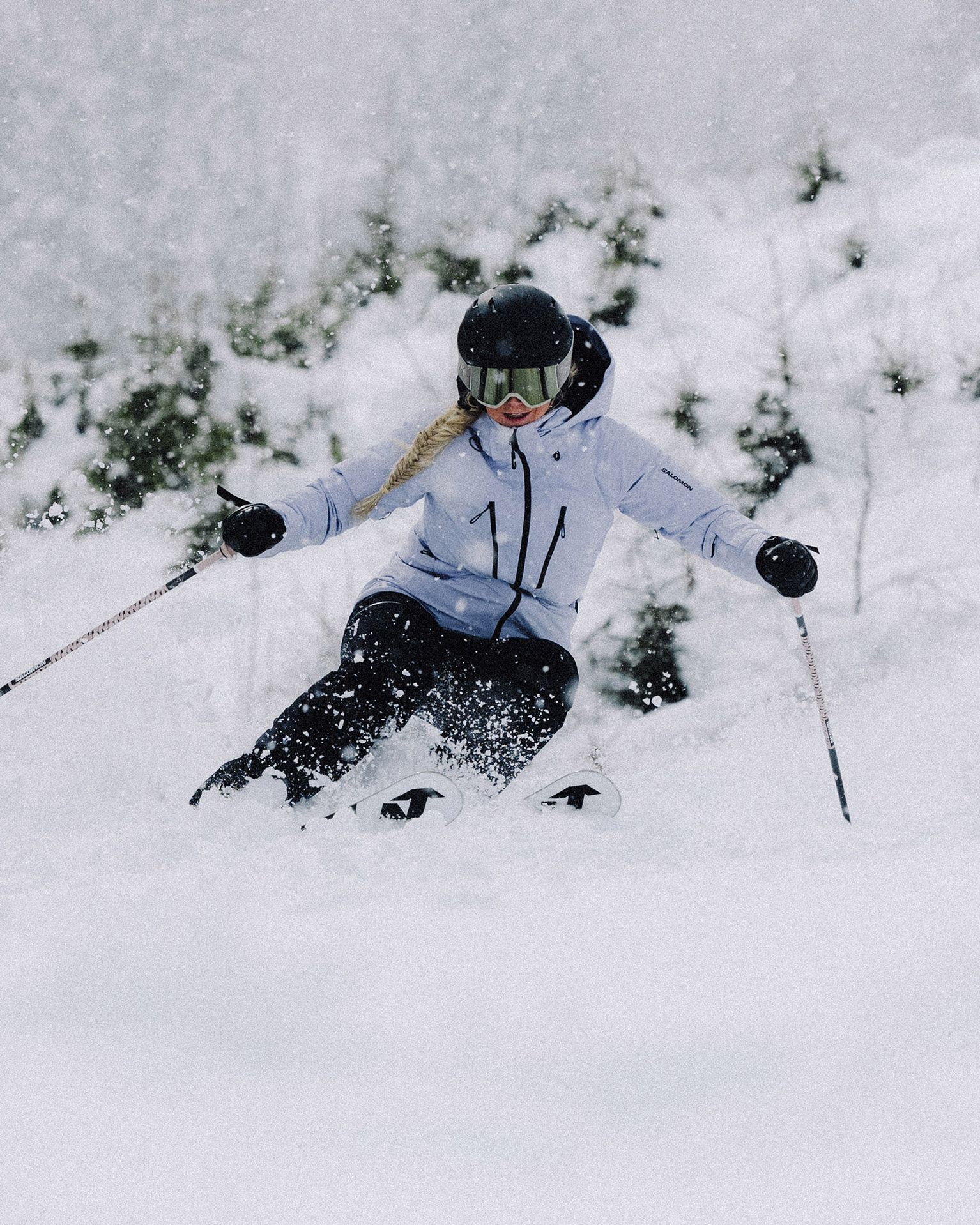 A skier in a white jacket and black pants navigates through fresh snow on a snowy slope, surrounded by snow-covered trees.
