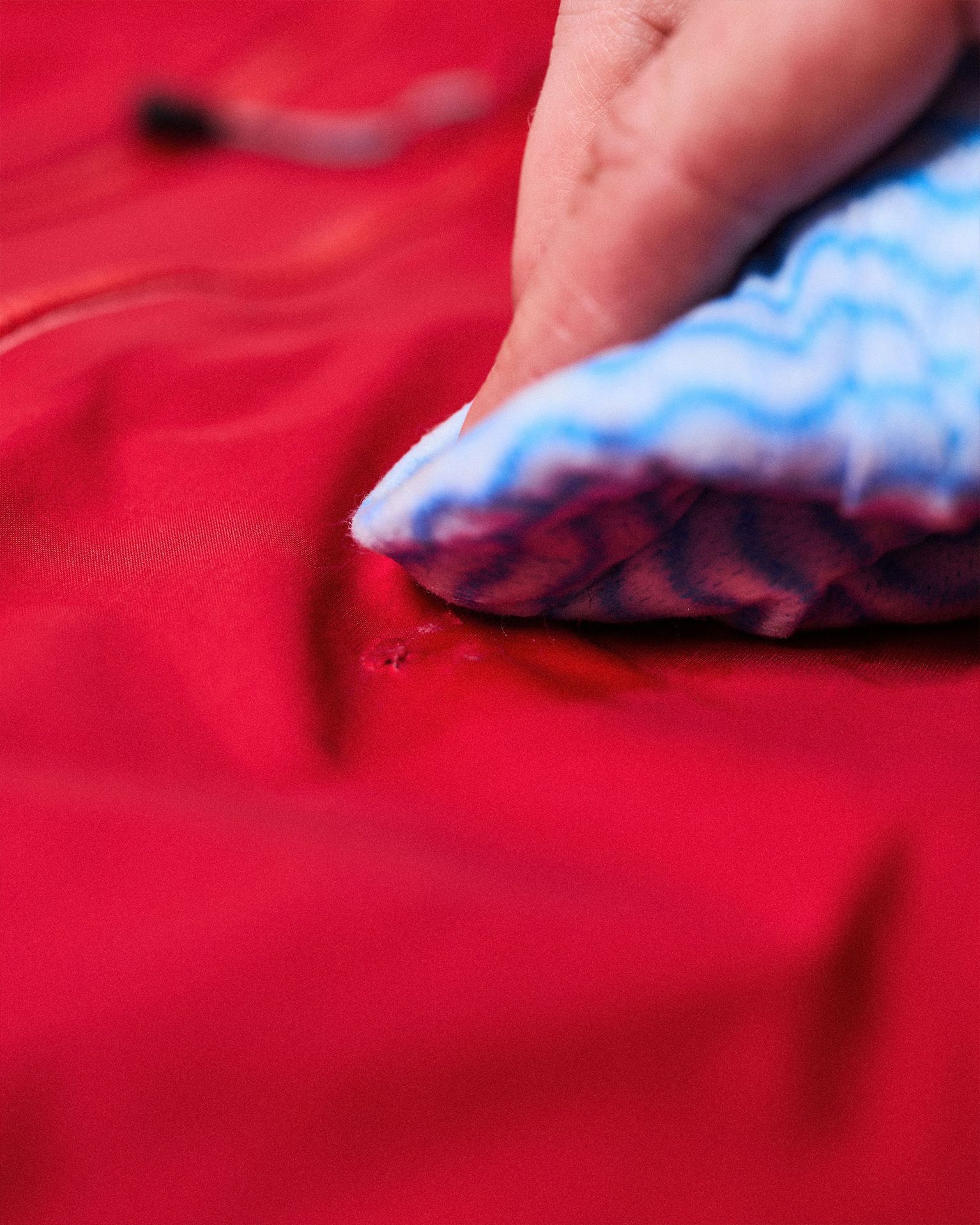 Hand cleaning a red waterproof jacket with a blue and white striped cloth.