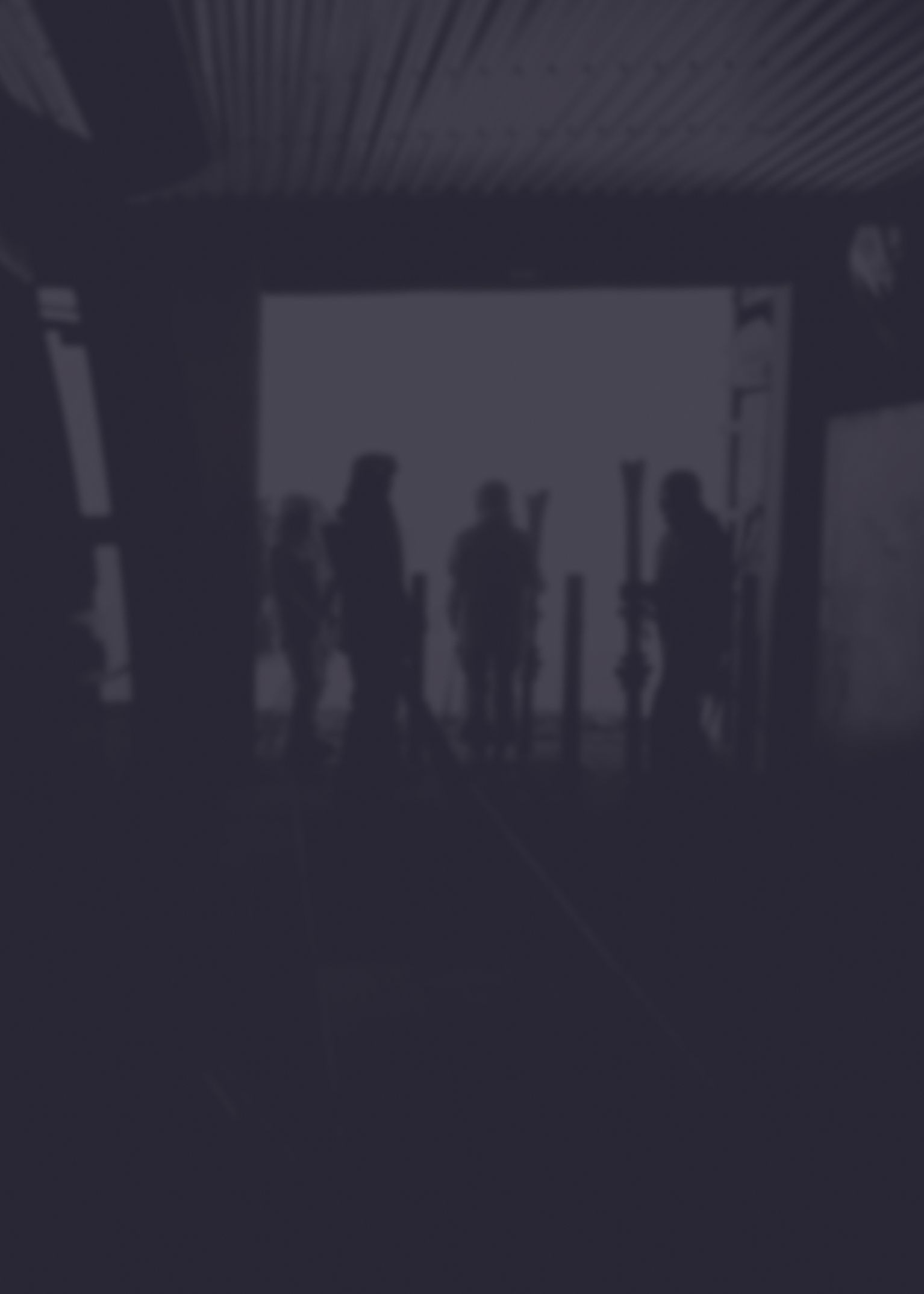 Silhouettes of people with ski gear inside a dimly lit building, facing an open doorway with bright light outside.