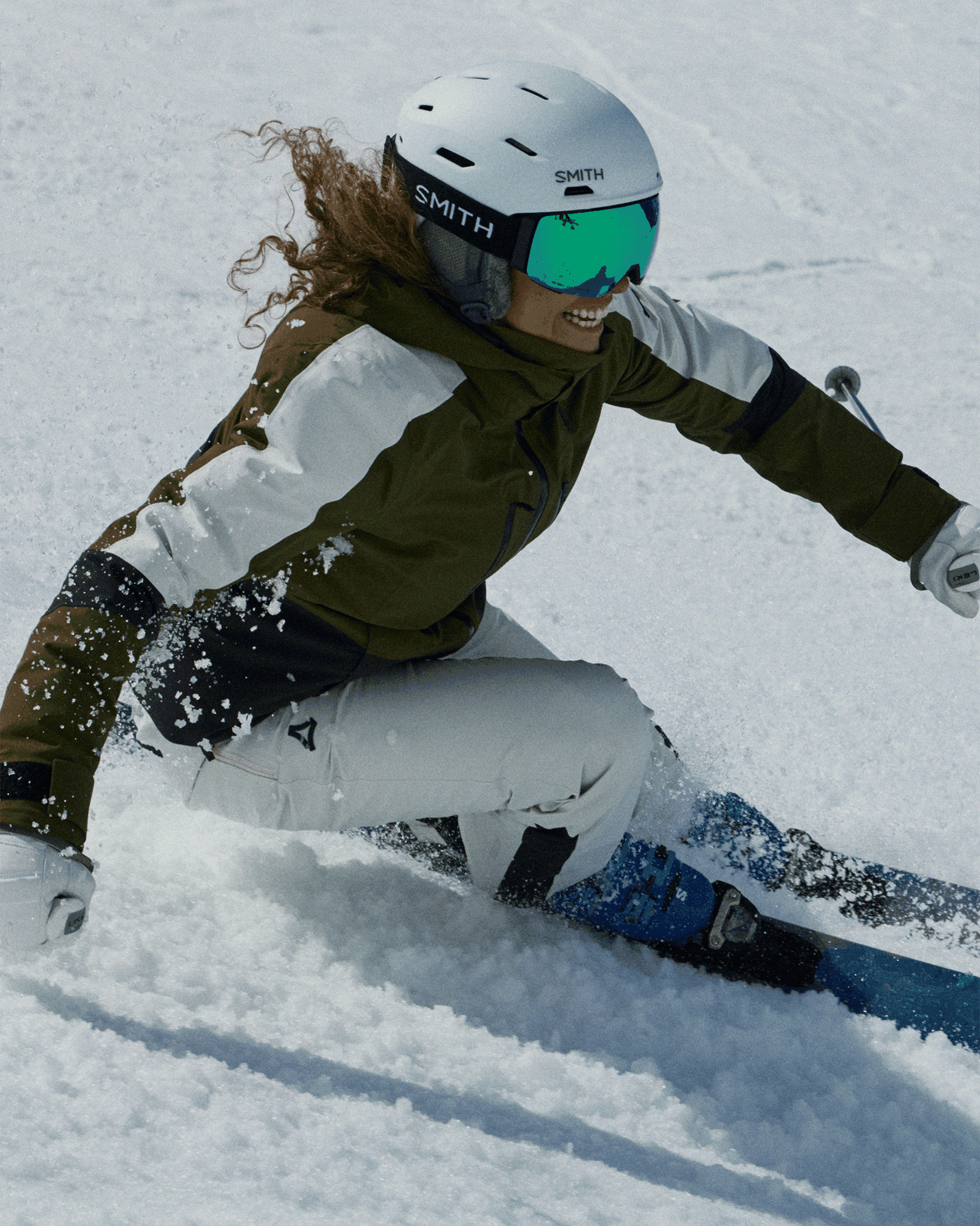 A skier in green and white gear carves through the snow, wearing a white helmet and reflective goggles, exuding confidence and skill.