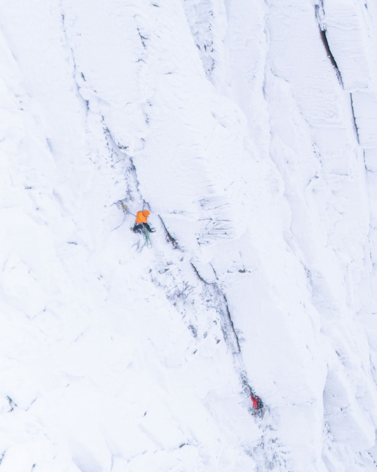 Aerial view of climbers in bright gear ascending a snow-covered mountain slope, showcasing challenging icy terrain.