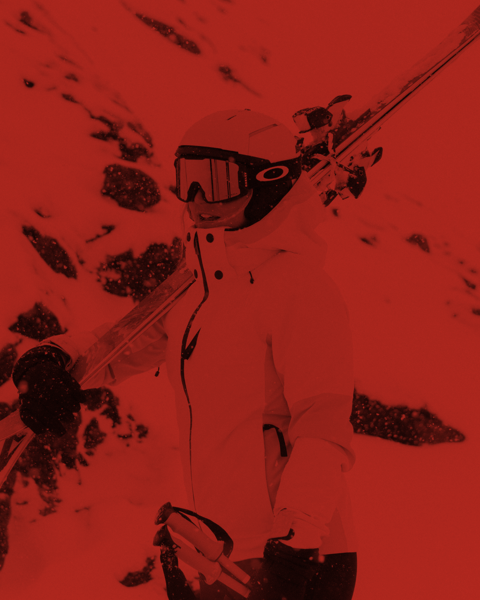 Person in a ski jacket and goggles holds skis against a snowy mountain backdrop.