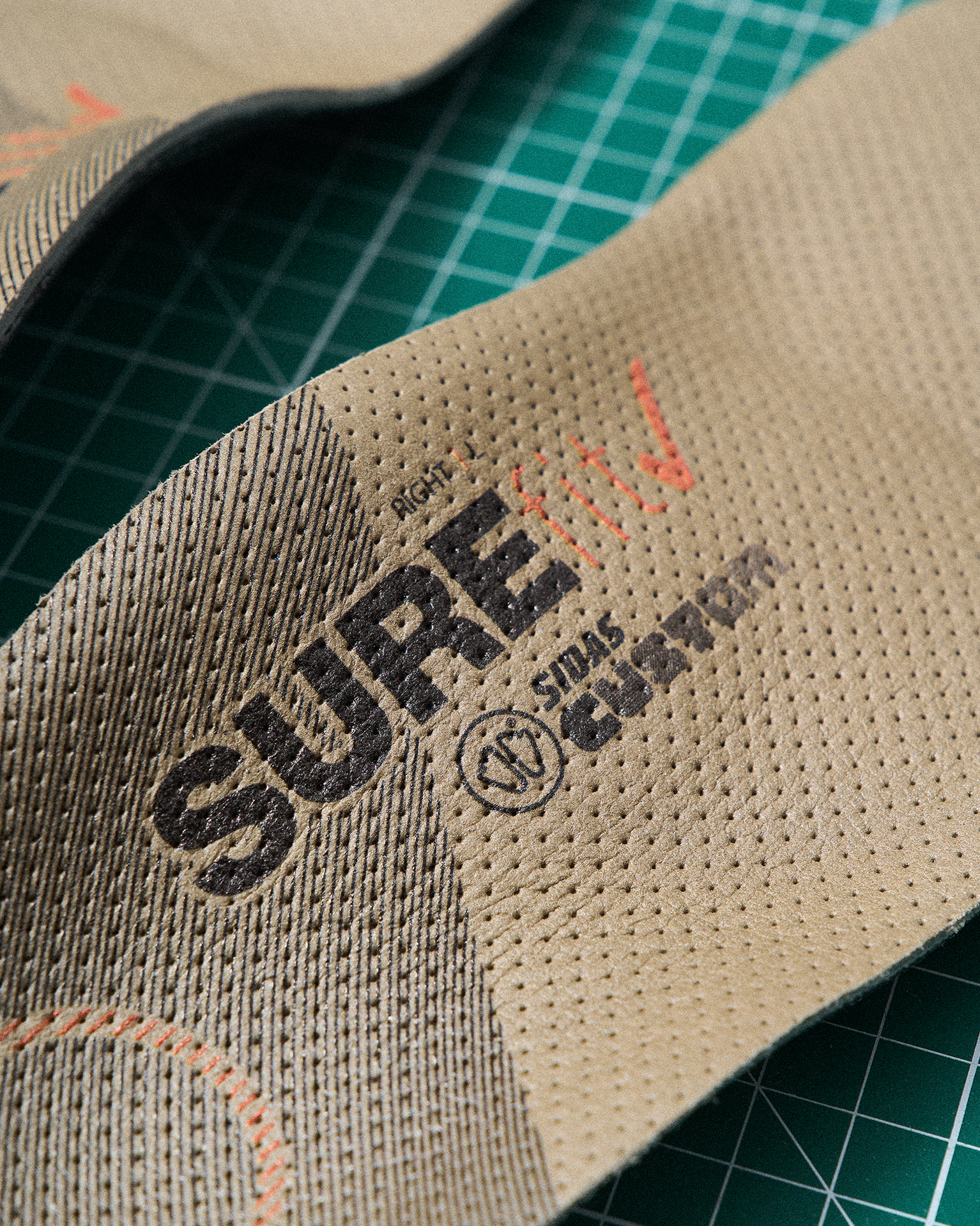Close-up of a textured insole with "SURE" and "CUSTOM" printed, placed on a green grid cutting mat.