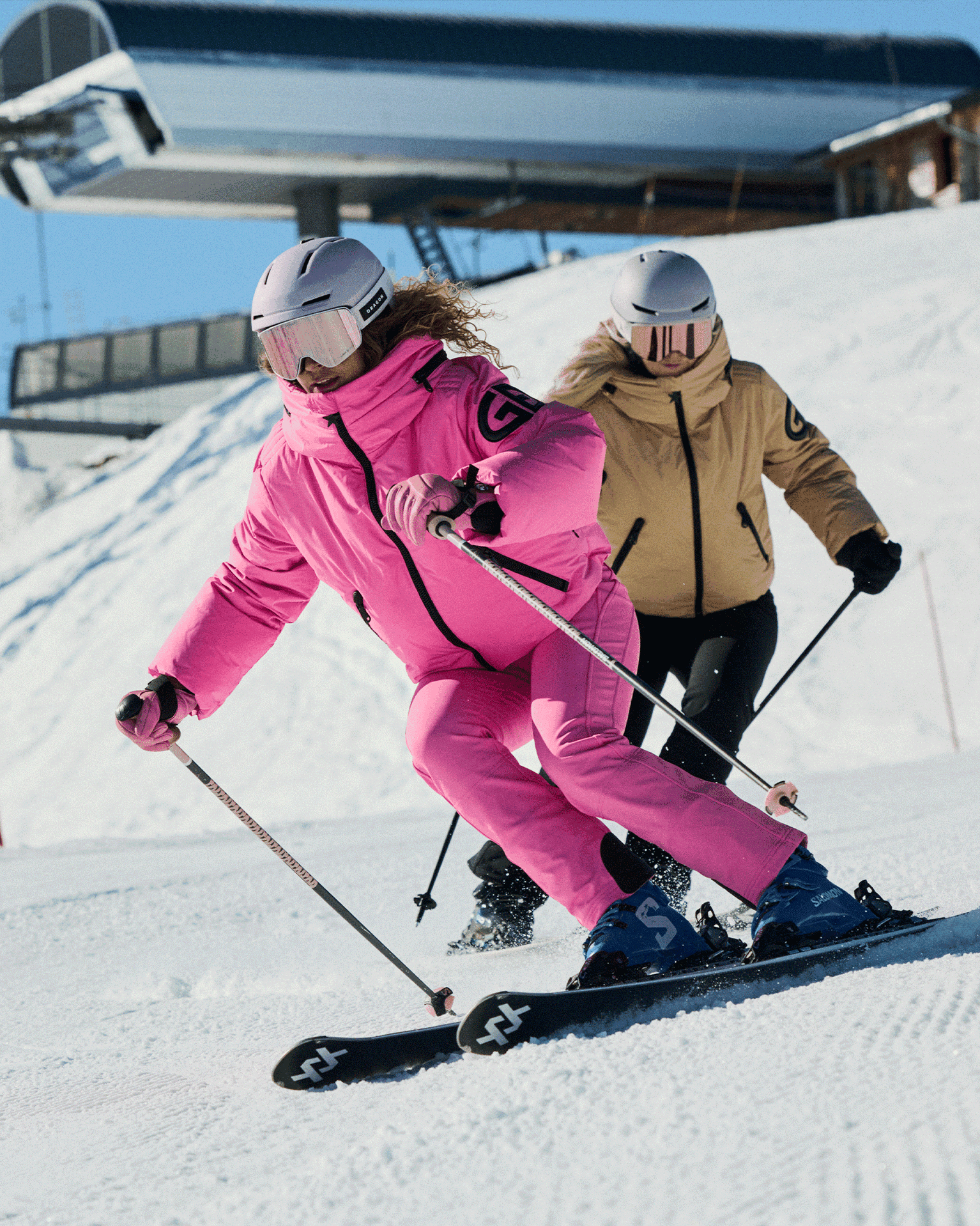 Two skiers in bright jackets glide confidently down a snowy slope.
