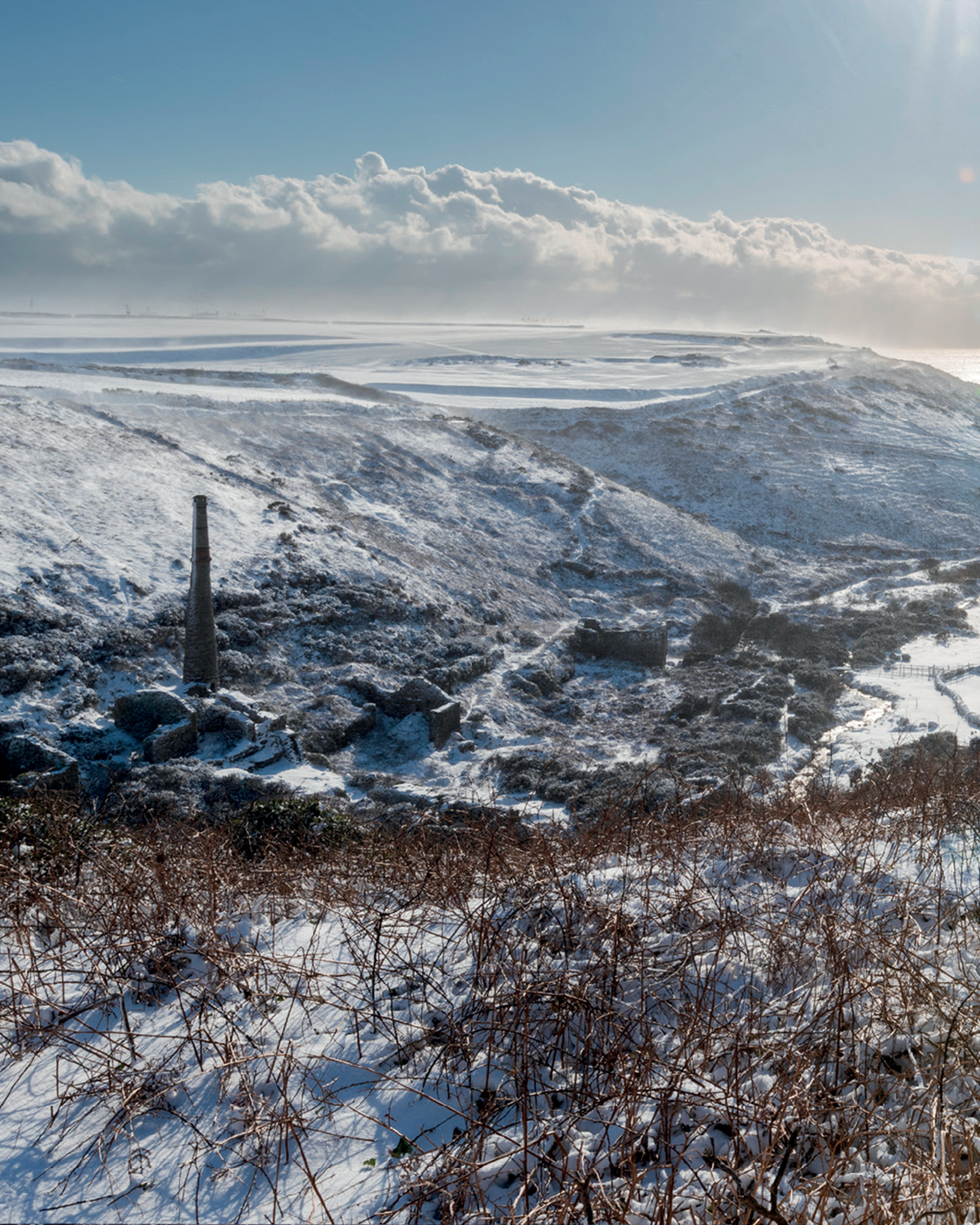 Snow-covered hills with ruins, and dramatic clouds under a clear blue sky.