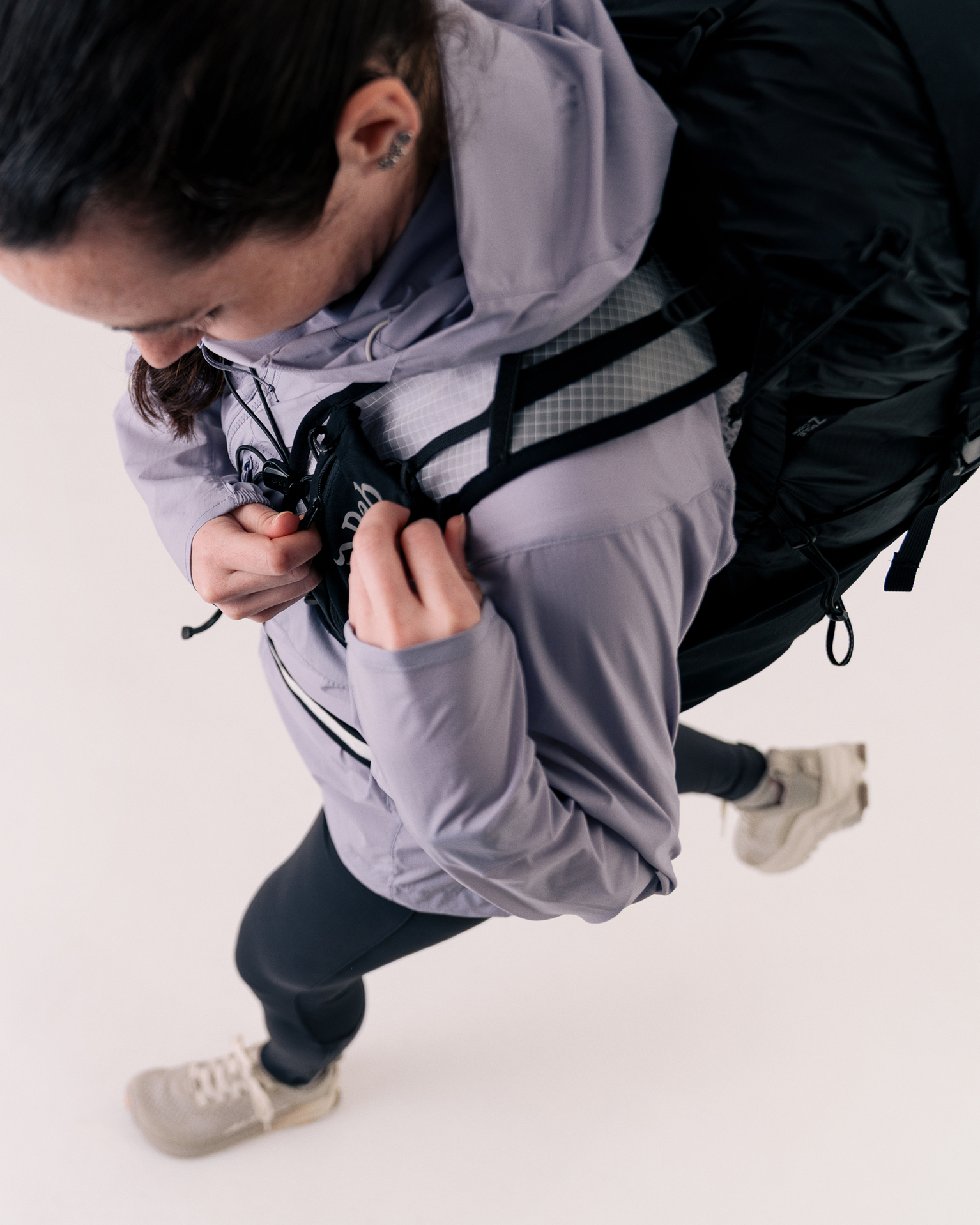 Person wearing a purple jacket and black backpack, captured from above, walking confidently in a studio setting.