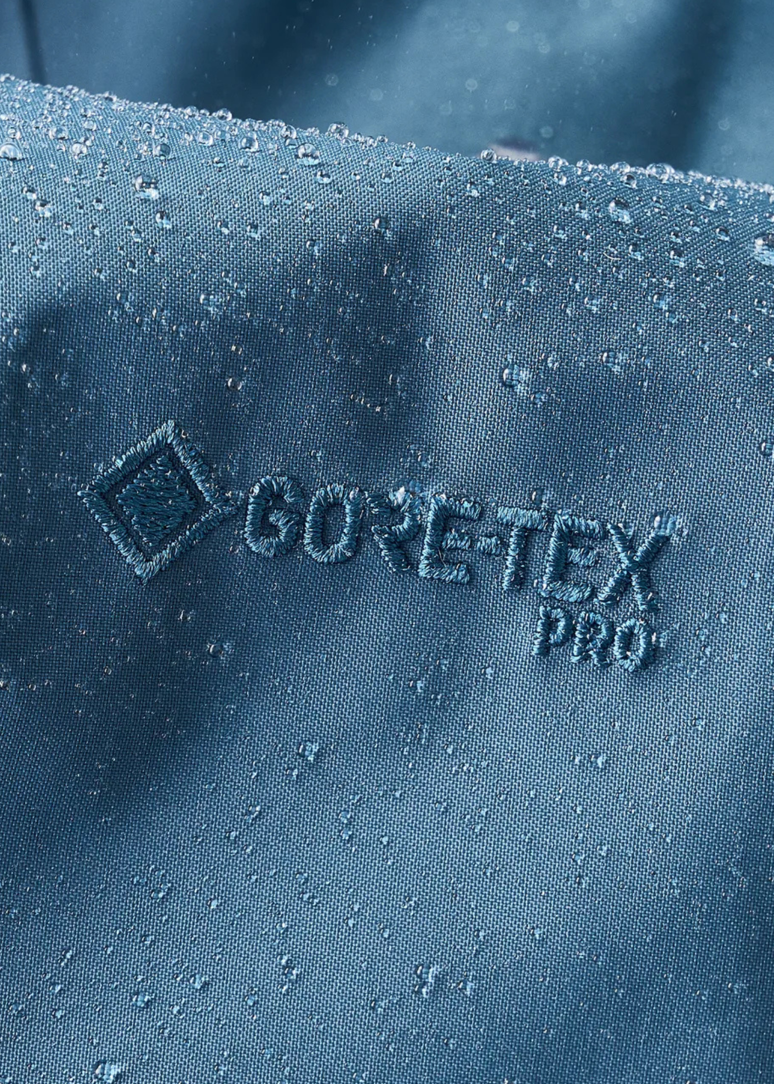 Close-up of blue GORE-TEX Pro fabric with water droplets beading on the surface, showcasing its waterproof properties.