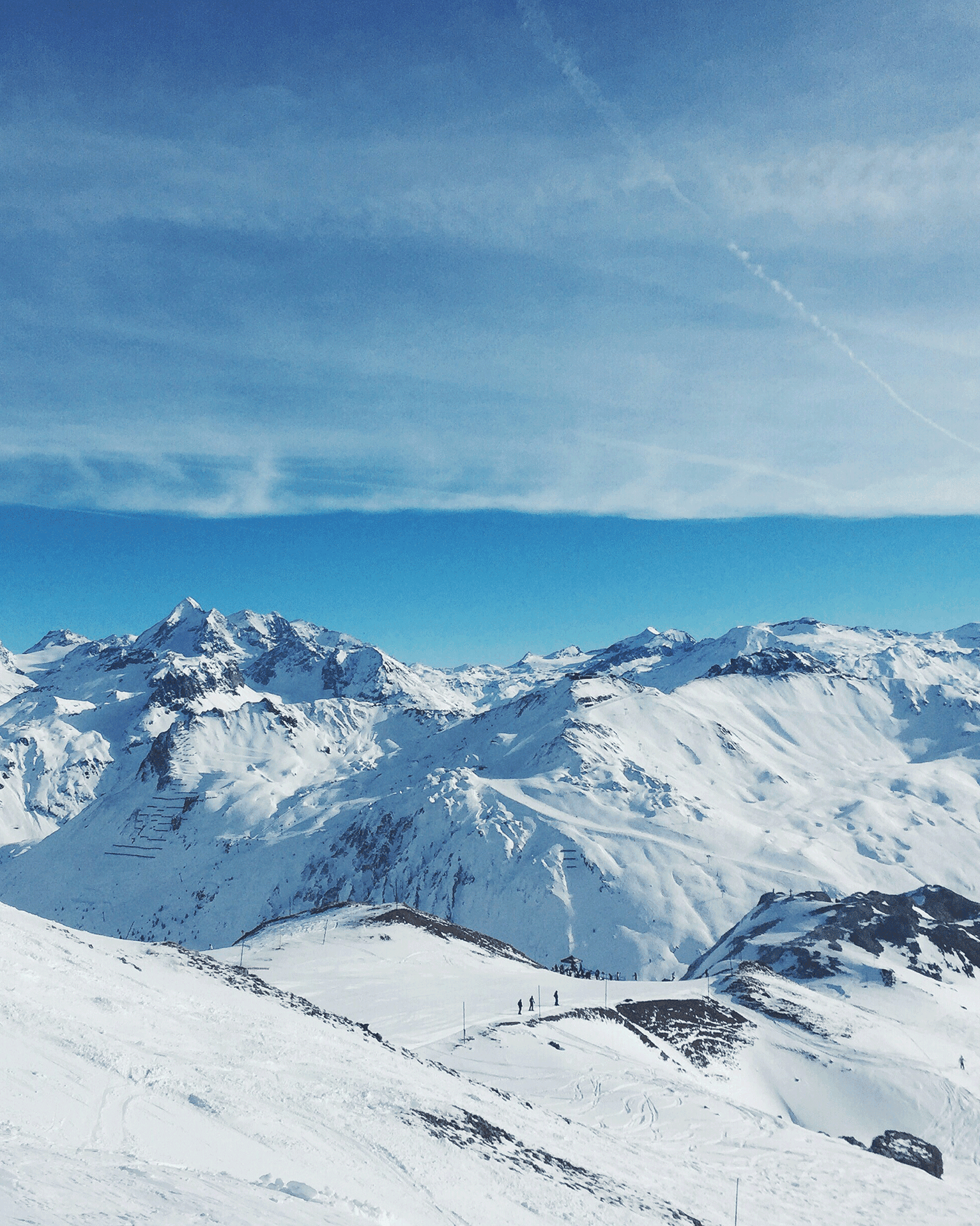 Expansive view of snow-covered mountains under a clear blue sky with distant skiers.