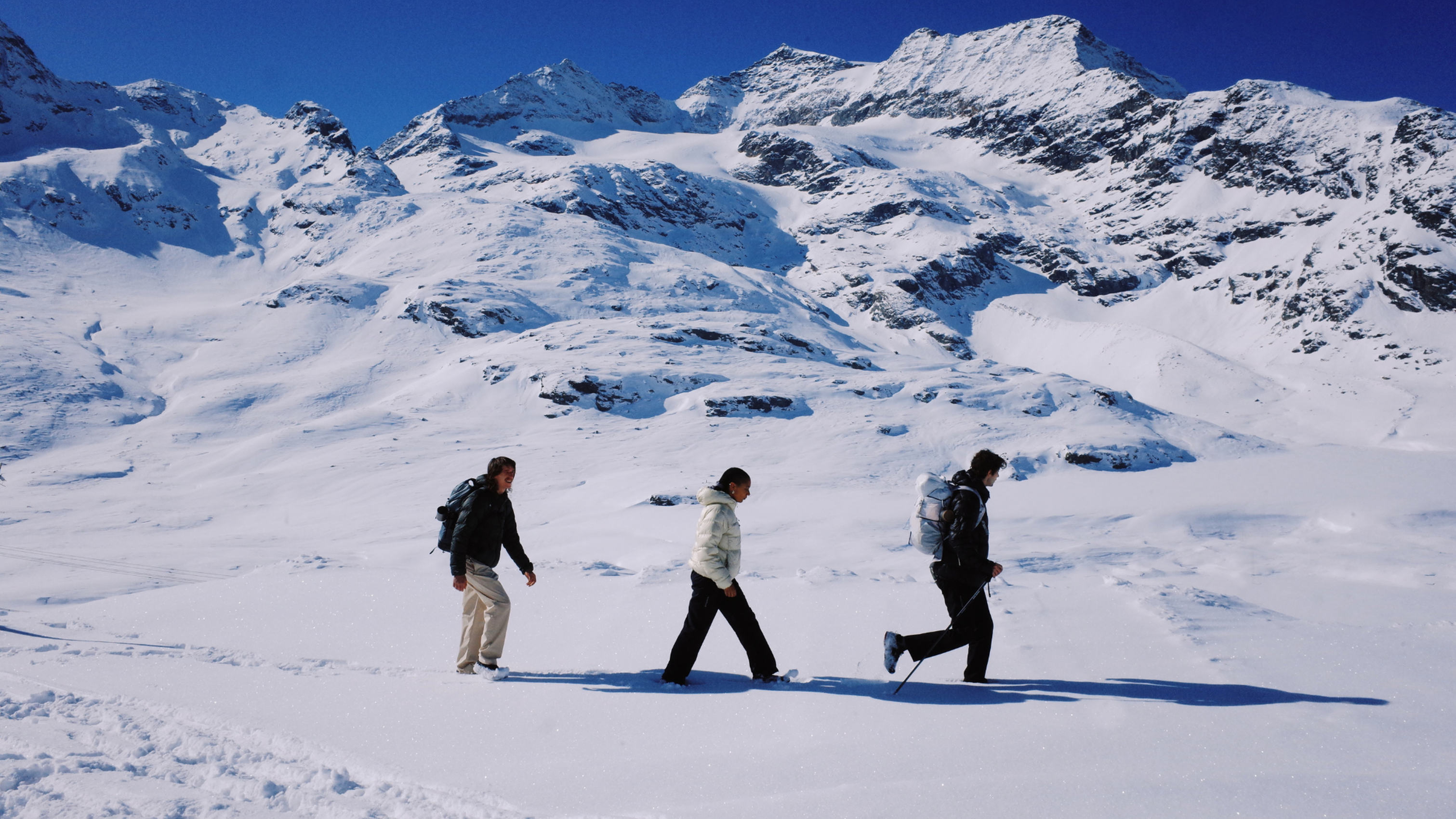 Three people walk though a snowy landscape