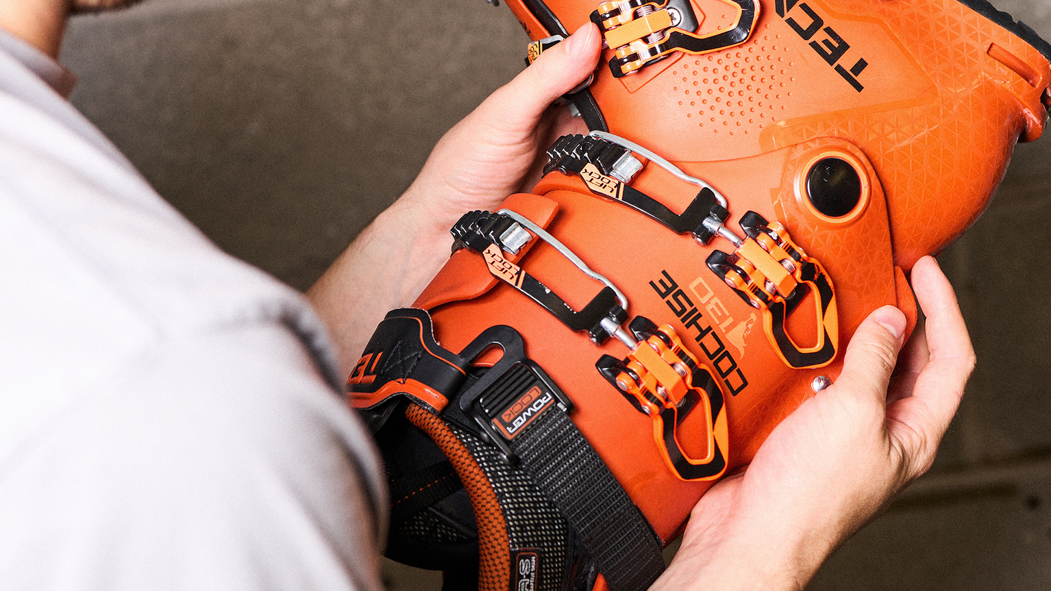 Person holding an orange ski boot with black and silver buckles, featuring the brand name and logo.