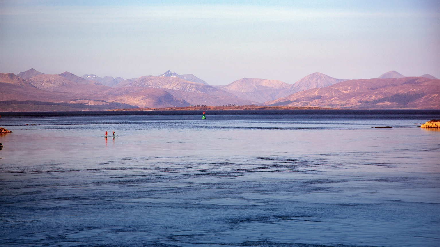 View of people paddleboarding with mountains in the background