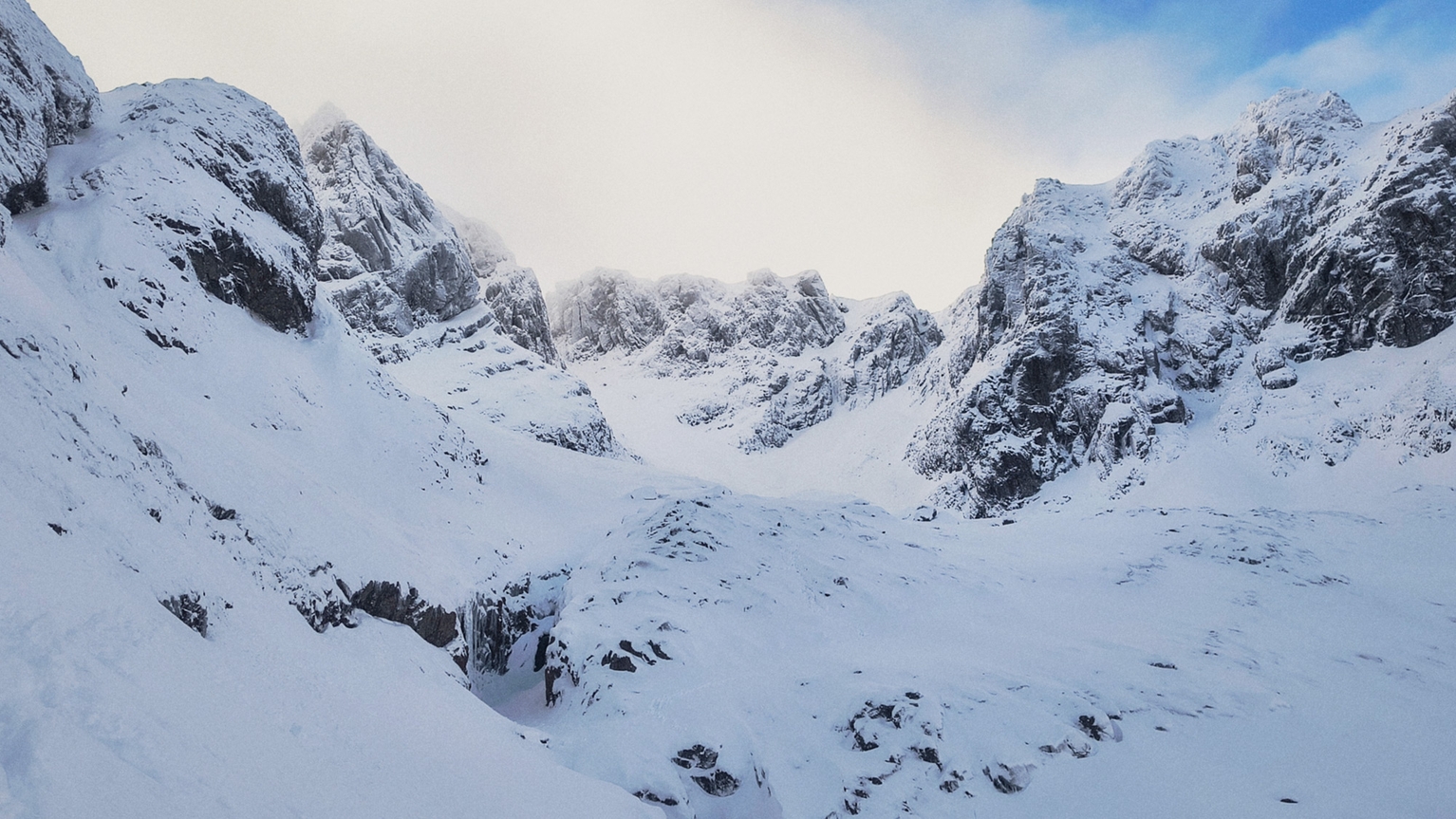 Snow-covered mountain range with rugged peaks under a clear blue sky, offering a serene and majestic winter landscape.
