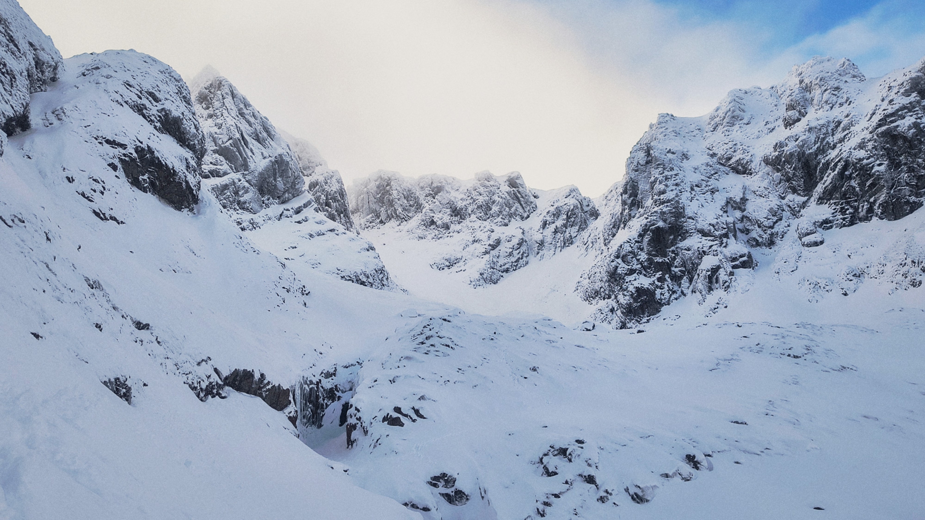 Snow-covered mountain range with rugged peaks under a clear blue sky, offering a serene and majestic winter landscape.