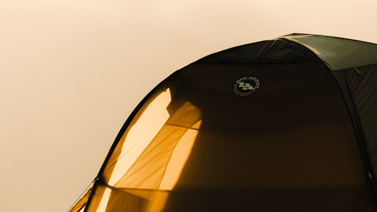Close-up of a tent illuminated by warm sunlight, highlighting brand logo against a tan background.