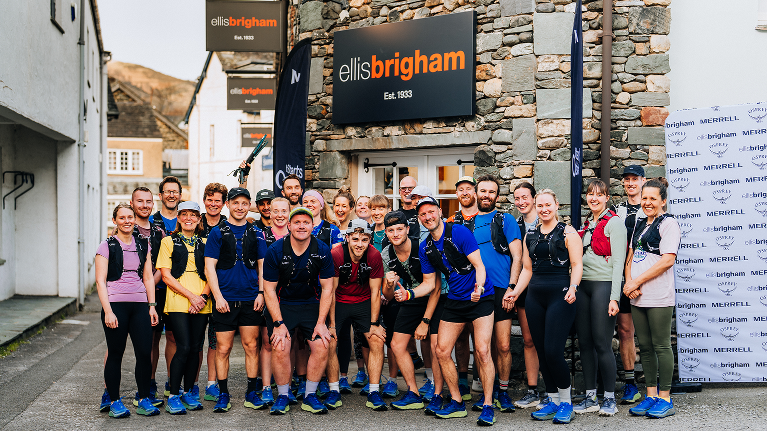 Group of people in athletic gear posing outside an Ellis Brigham shop. They appear ready for a mountain sports activity.
