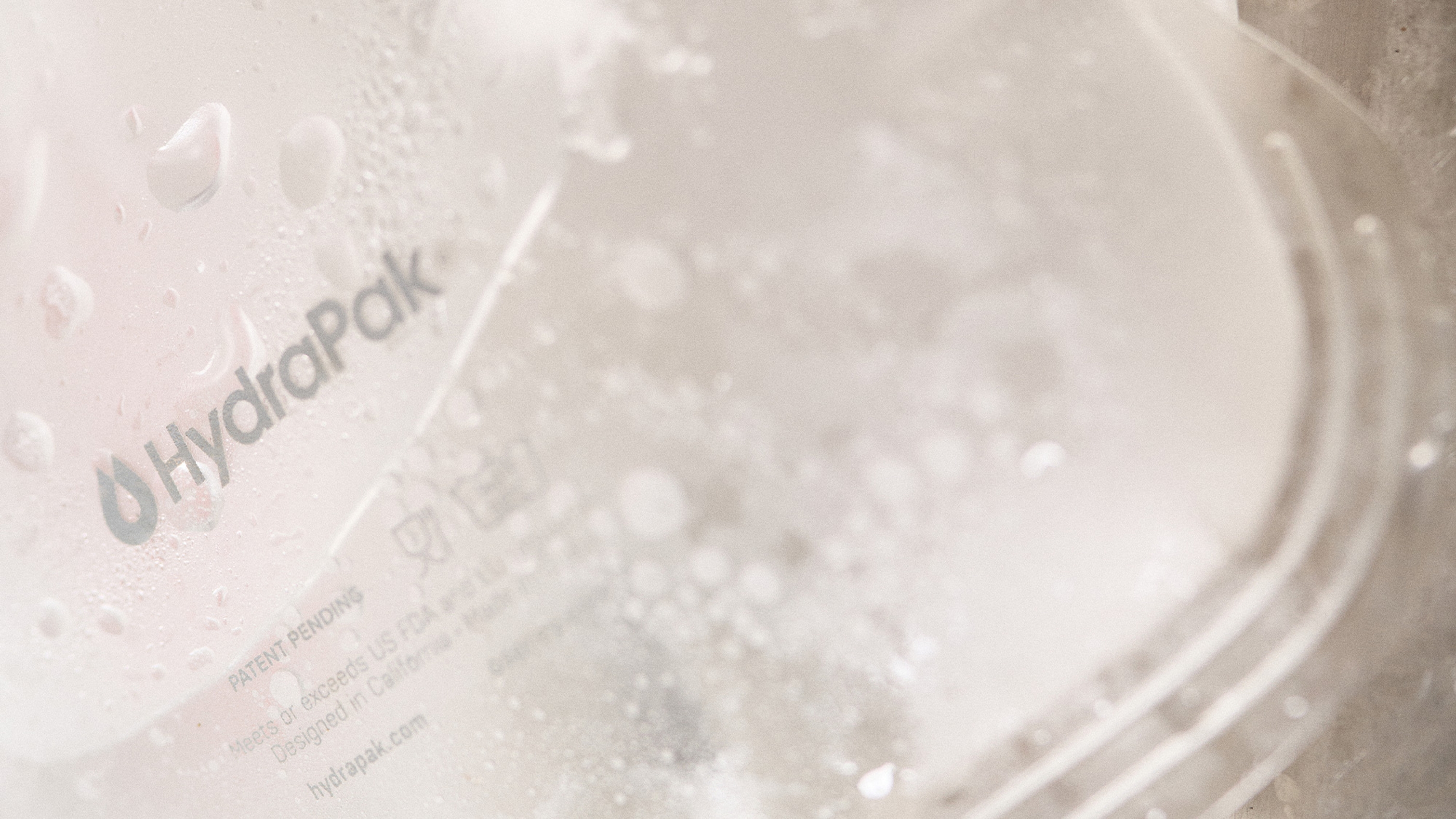 Close-up of a translucent HydraPak water reservoir with droplets, showcasing the brand logo and product details in soft focus.