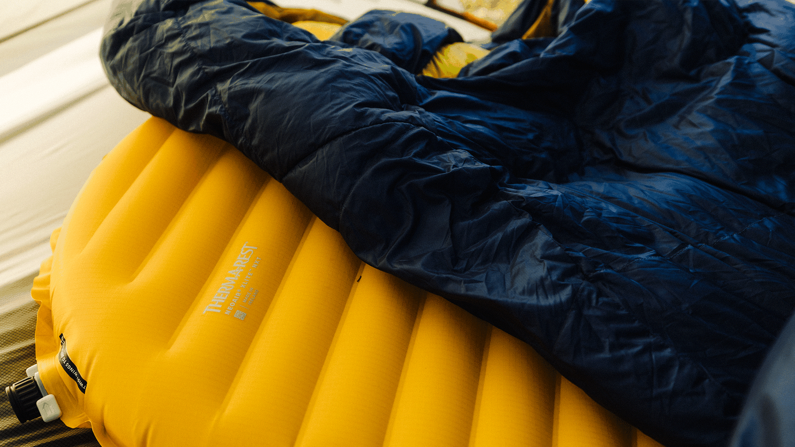 Yellow inflatable sleeping mat partially covered by a puffy dark blue sleeping bag, in a camping setup.