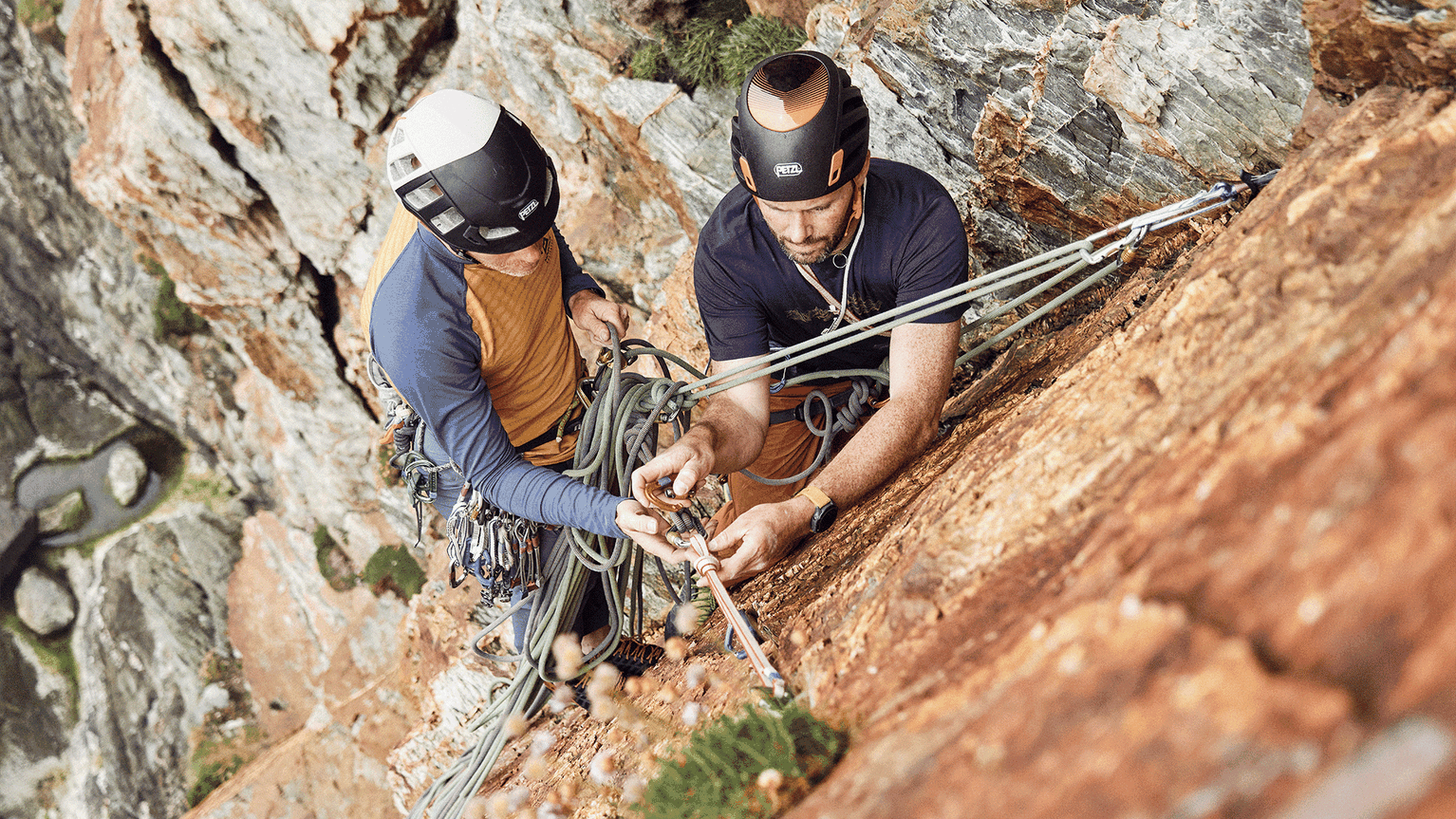 Two climbers securing ropes on a steep rock face, demonstrating teamwork and precision in a challenging mountain environment.