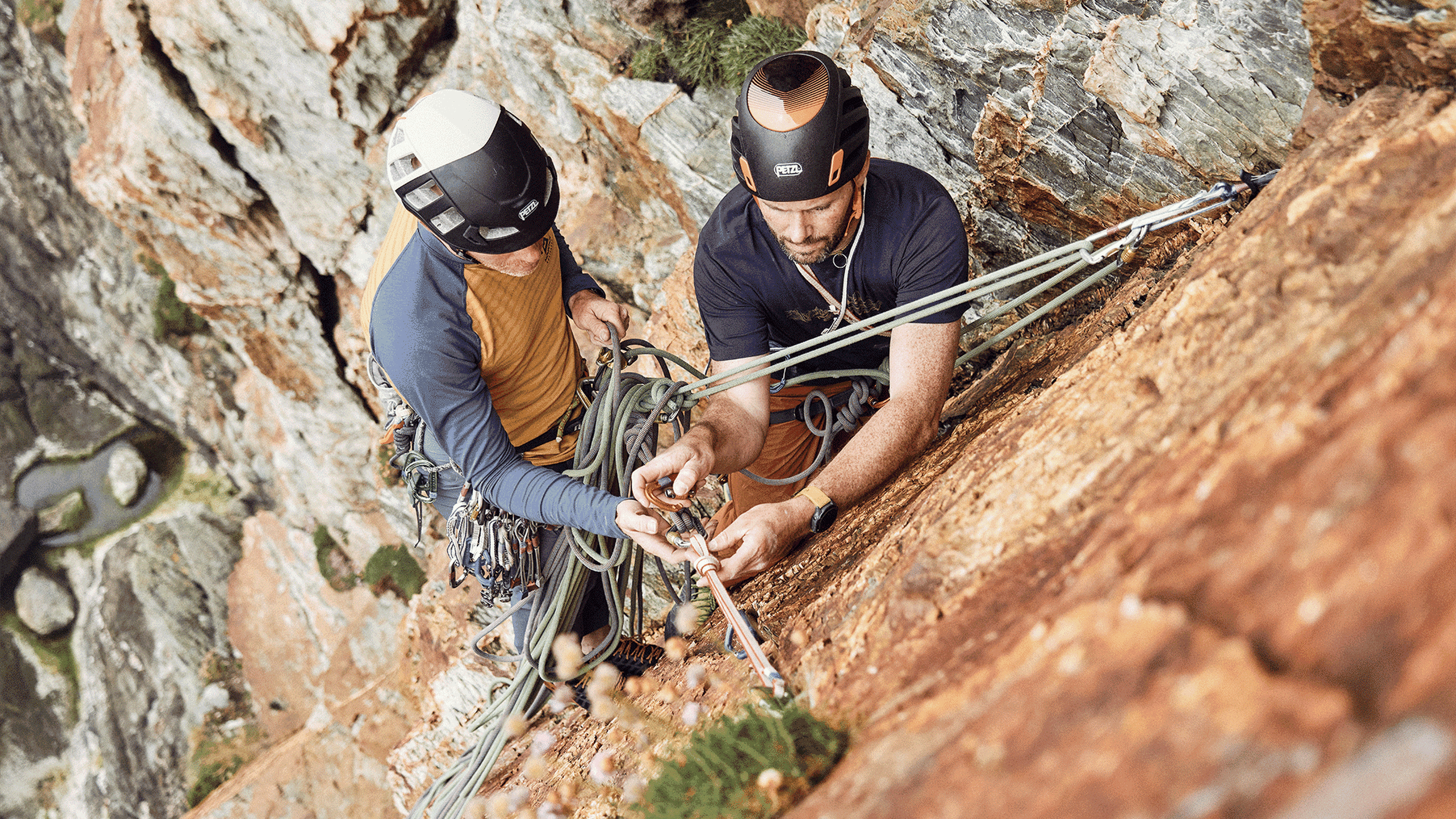 Two climbers securing ropes on a steep rock face, demonstrating teamwork and precision in a challenging mountain environment.