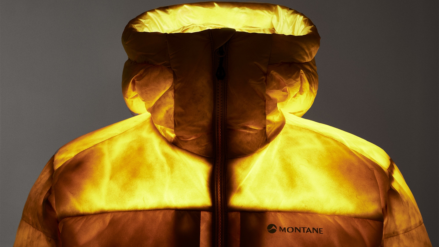 A bright yellow Montane down jacket with a hood, illuminated dramatically against a dark background.