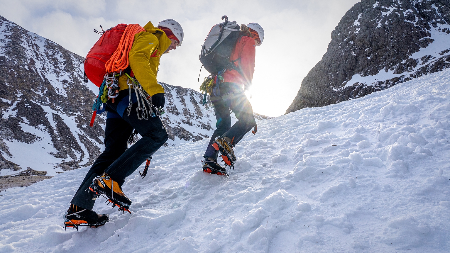 Two people walking up snowy hill wearing crampons