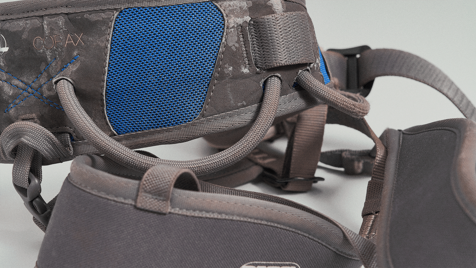 Close-up of a grey and blue climbing harness with adjustable straps and padding.