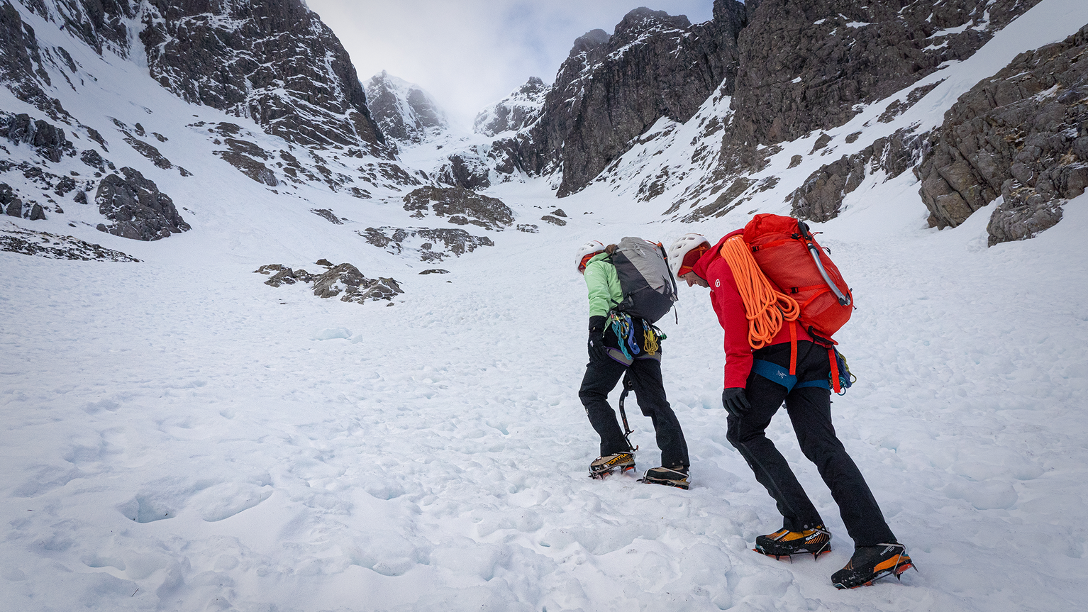 Two people walking up snowy hill wearing waterproof trousers