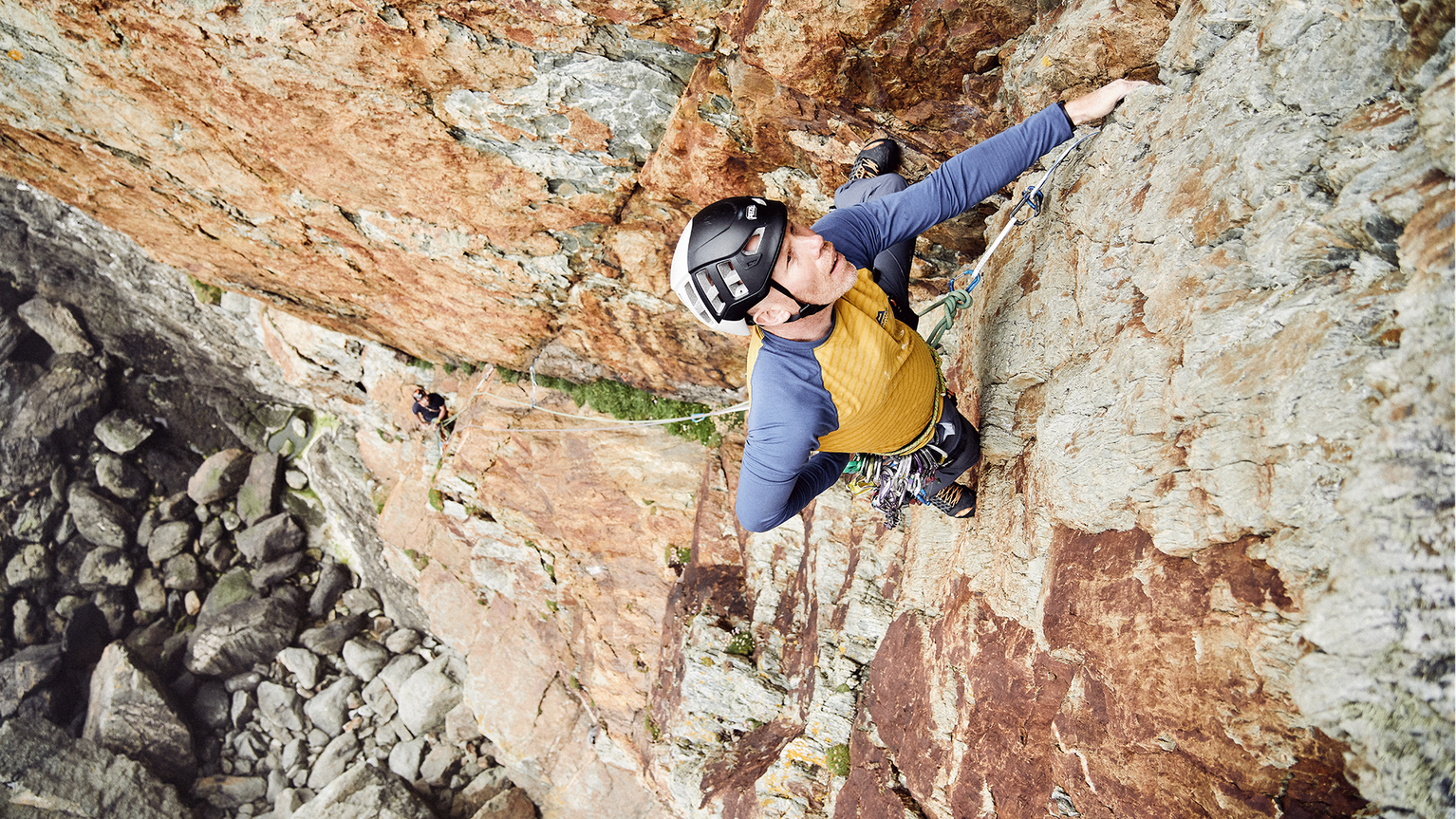 Climber in protective gear scaling a steep, rocky cliff face, showcasing determination and skill.