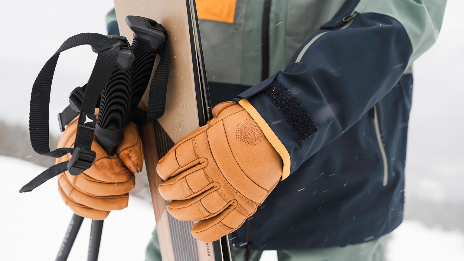 person wearing brown ski gloves holding their skis and poles
