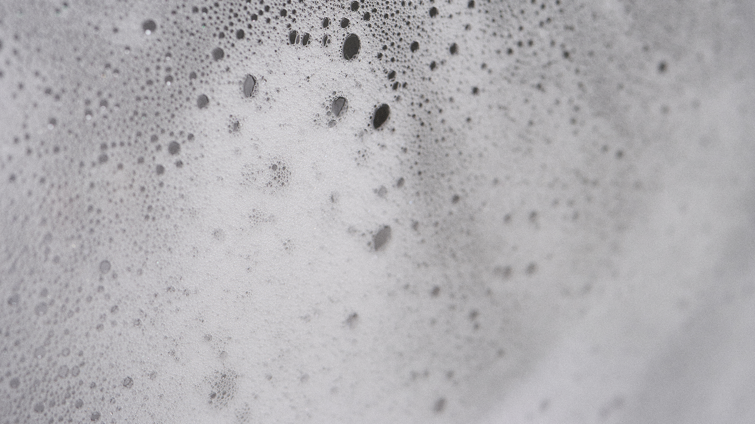 Close-up of white soap suds with various-sized bubbles on a smooth surface, creating a textured and foamy appearance.