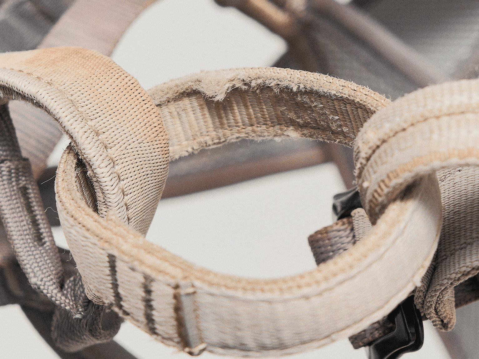 Close-up of well-worn climbing harness, showing frayed and textured straps with visible stitching details.