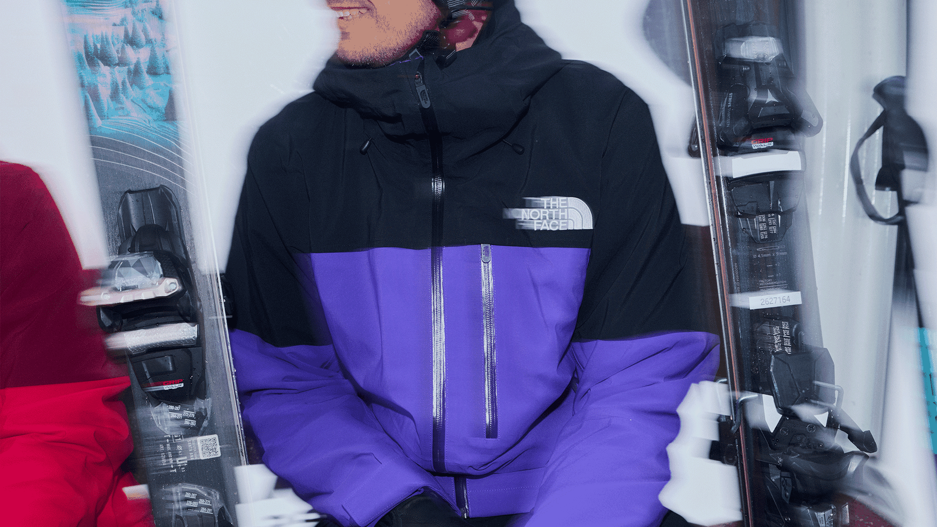 Person in a purple and black jacket smiling, sitting beside skis.