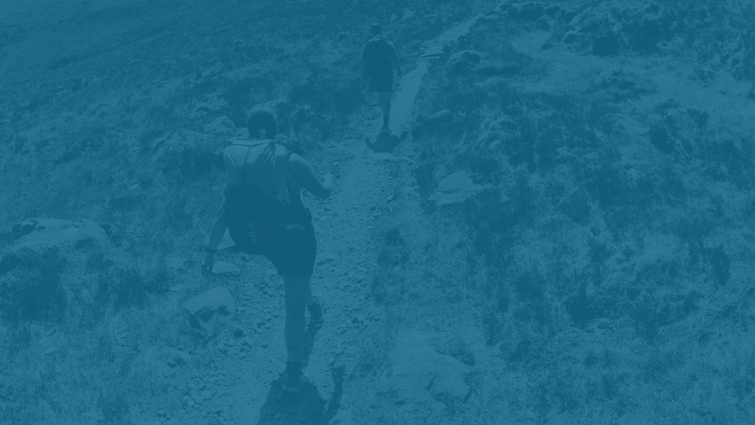 Two hikers on a mountain trail, wearing backpacks, navigating rocky terrain.