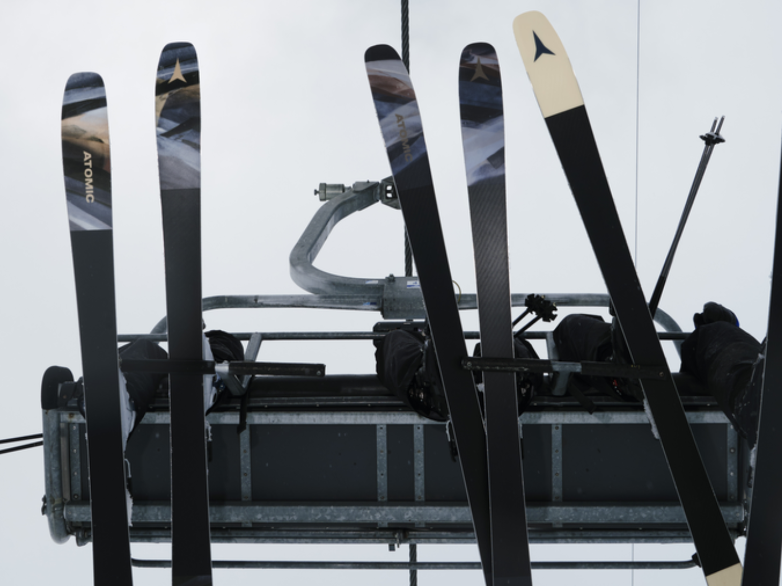 Ski lift with several pairs of skis attached, viewed from below against a cloudy sky.