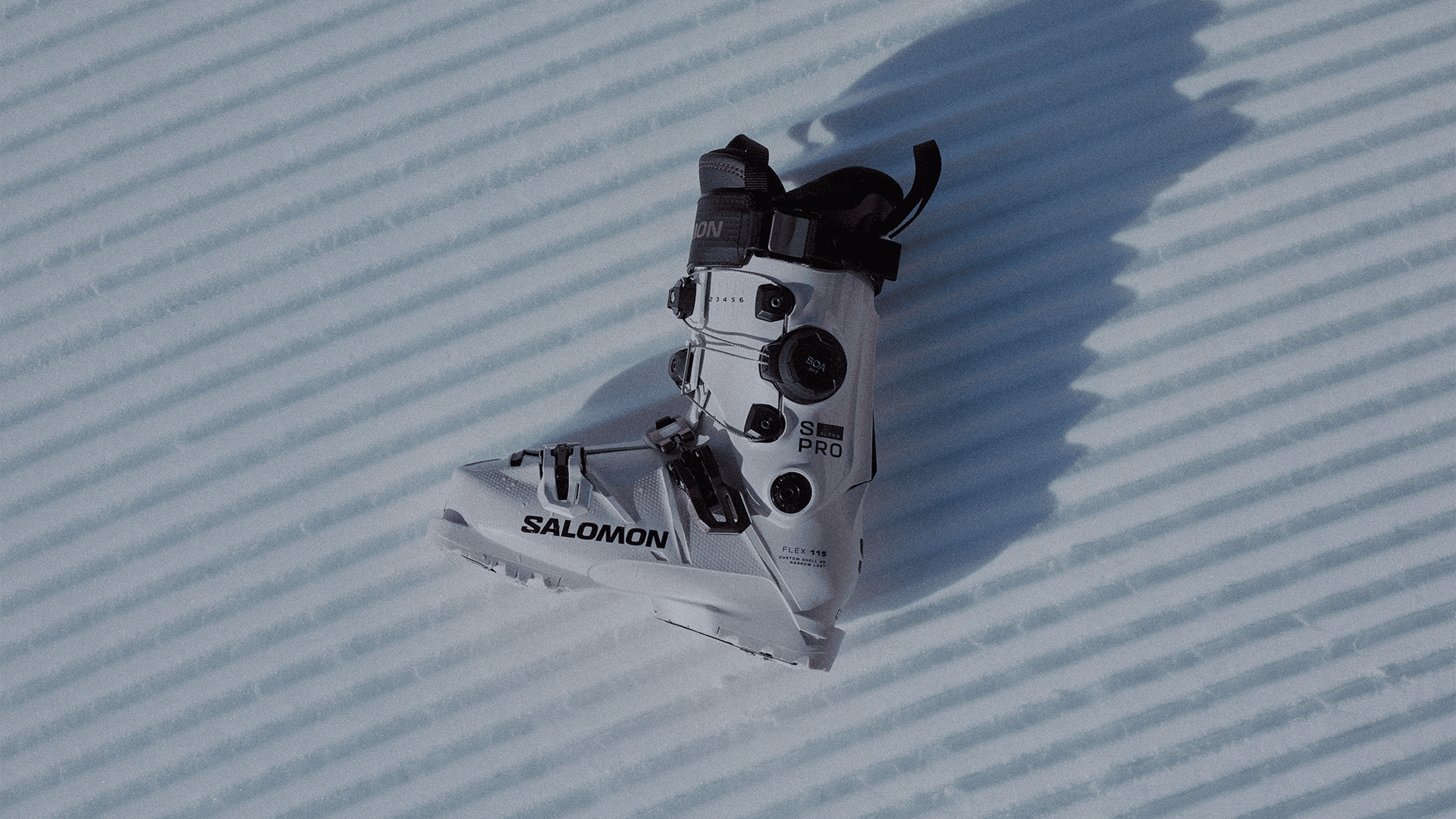 White ski boot with black and orange accents on textured snow, featuring the Salomon logo and BOA adjustment system.