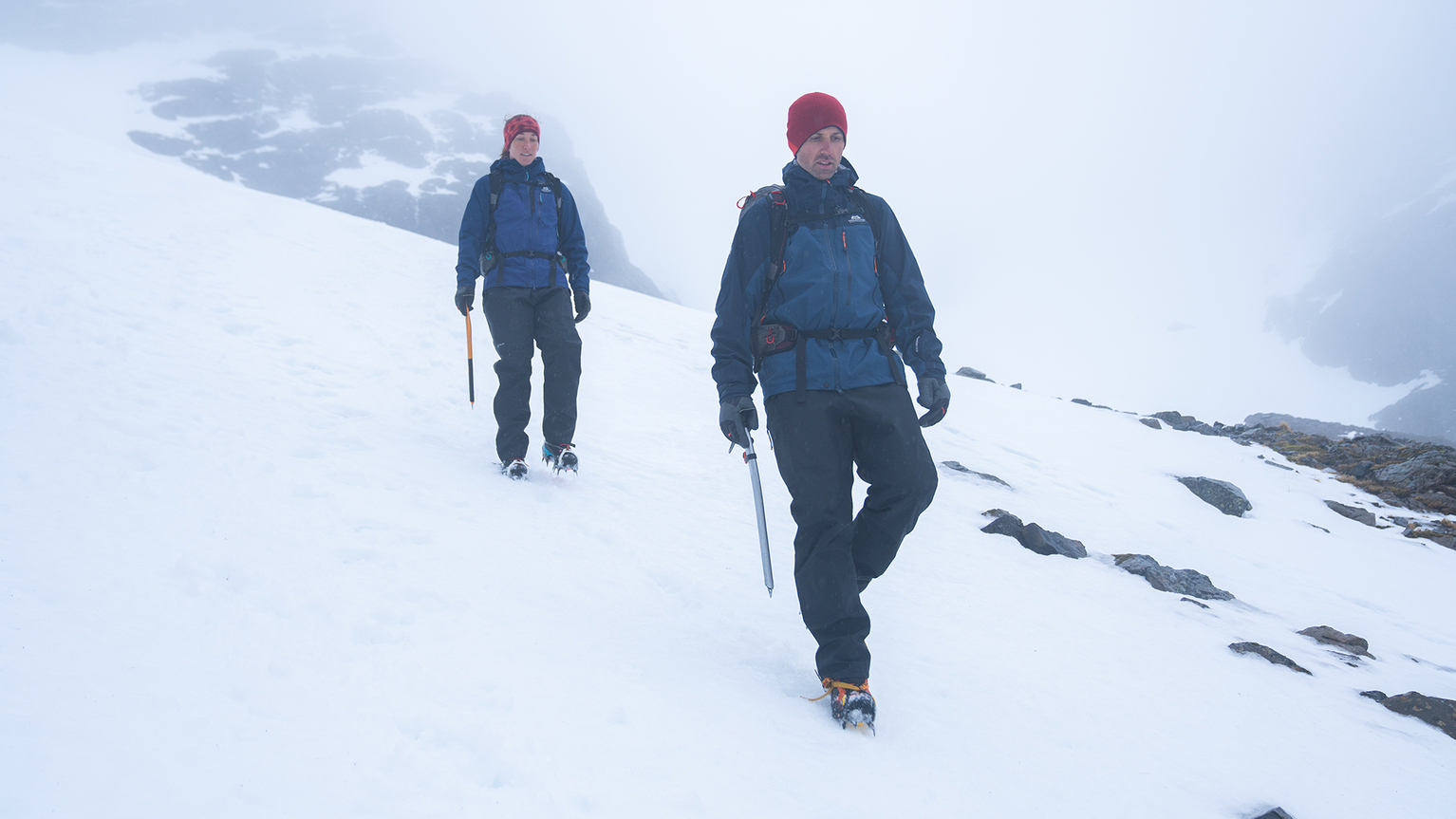 two people walking down snowy hill wearing crampons
