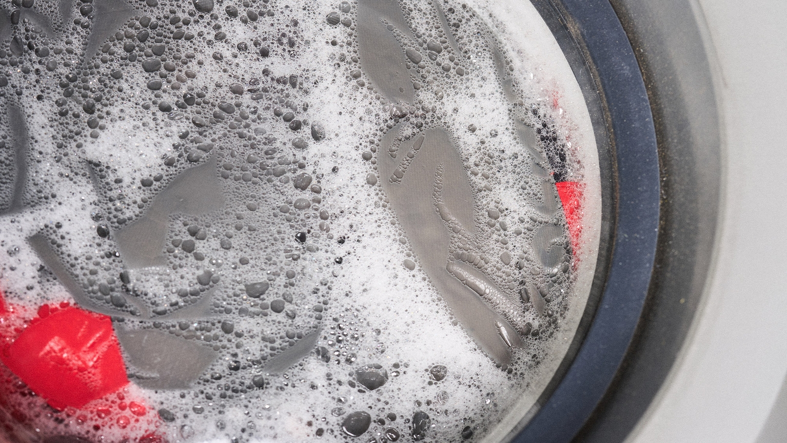 Close-up of a washing machine with soapy water, showing a red jacket being washed.