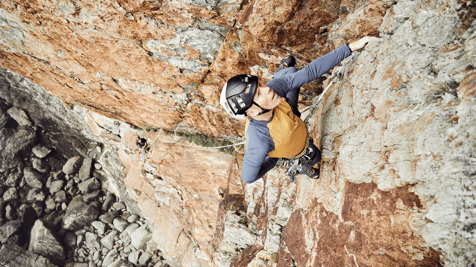Climber scales a vertical rock face. Wearing a helmet and yellow top, the climber navigates the challenging terrain.