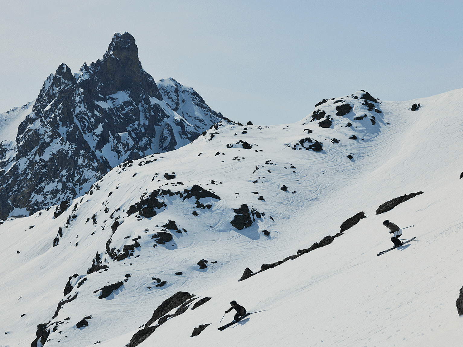 Skier navigating a snowy mountain slope with rugged peaks in the background.